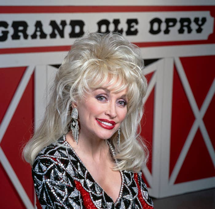 Person with voluminous hair and sparkly outfit, smiling in front of a "Grand Ole Opry" backdrop
