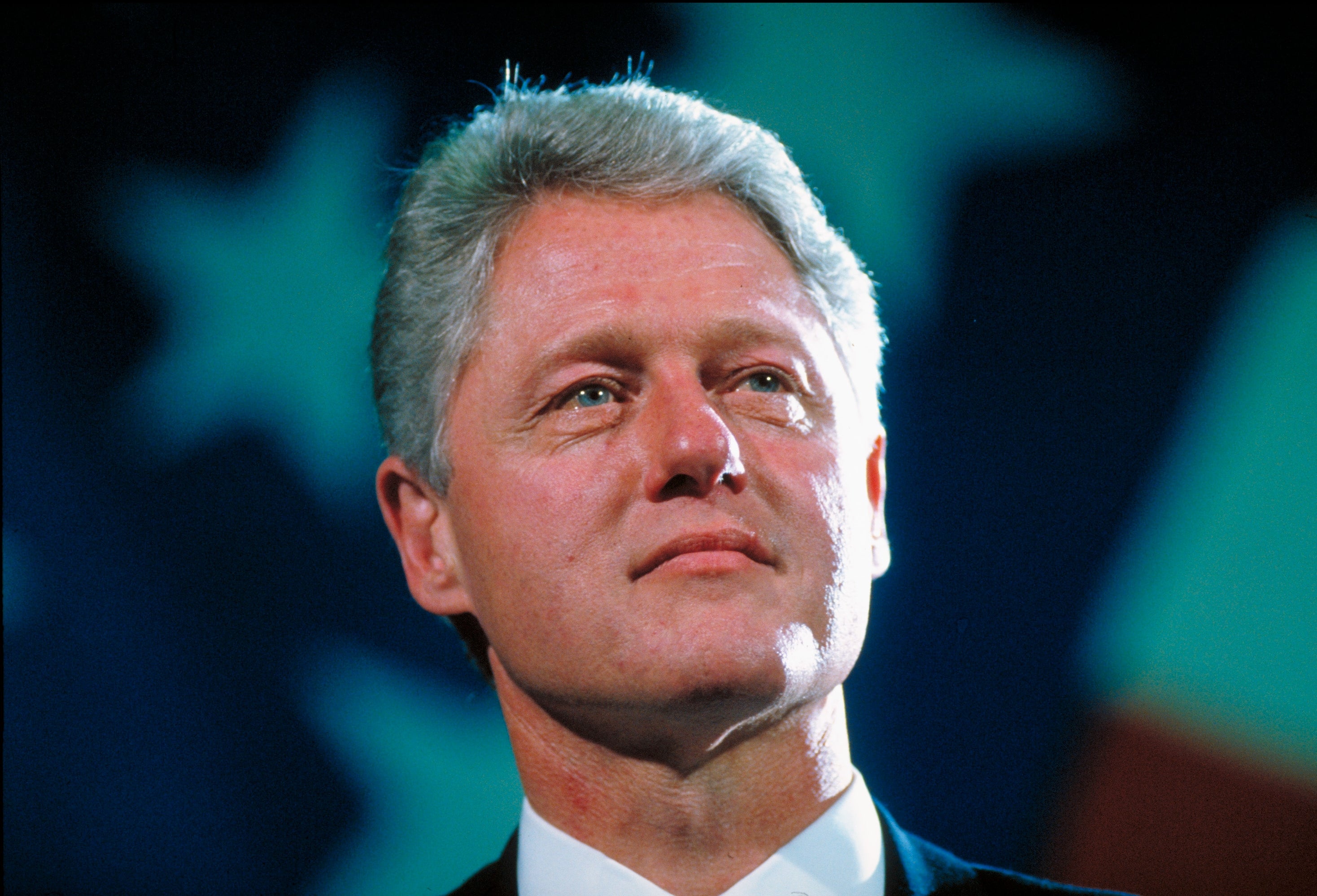 A person in a suit looks upward with a thoughtful expression, against a backdrop featuring abstract star shapes