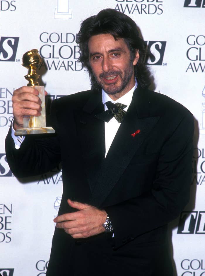 Person in a tuxedo holding a Golden Globe award, standing in front of a backdrop with event logos
