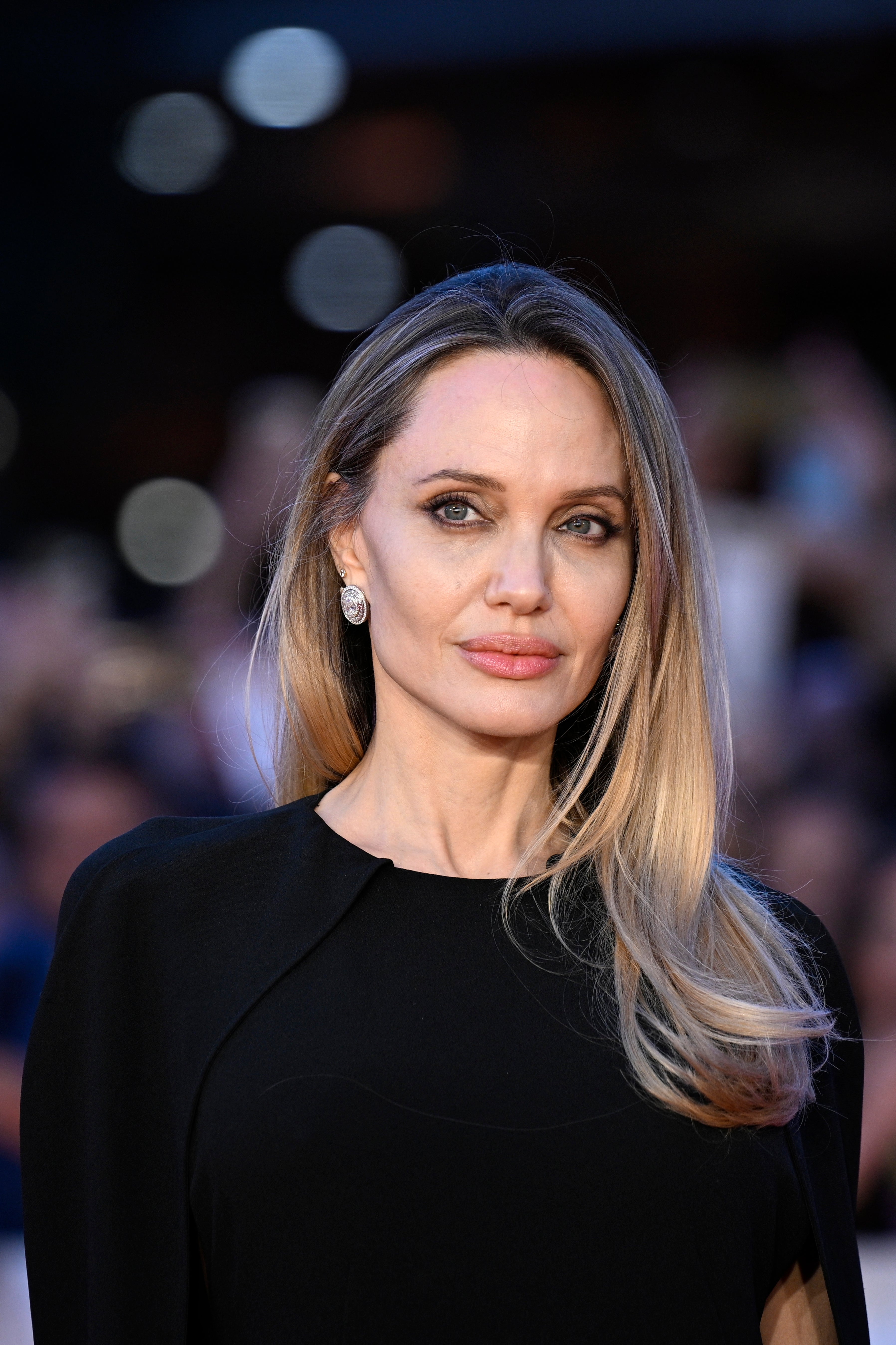 A person on a red carpet wearing a sleek, elegant gown with understated jewelry, posing with a neutral expression