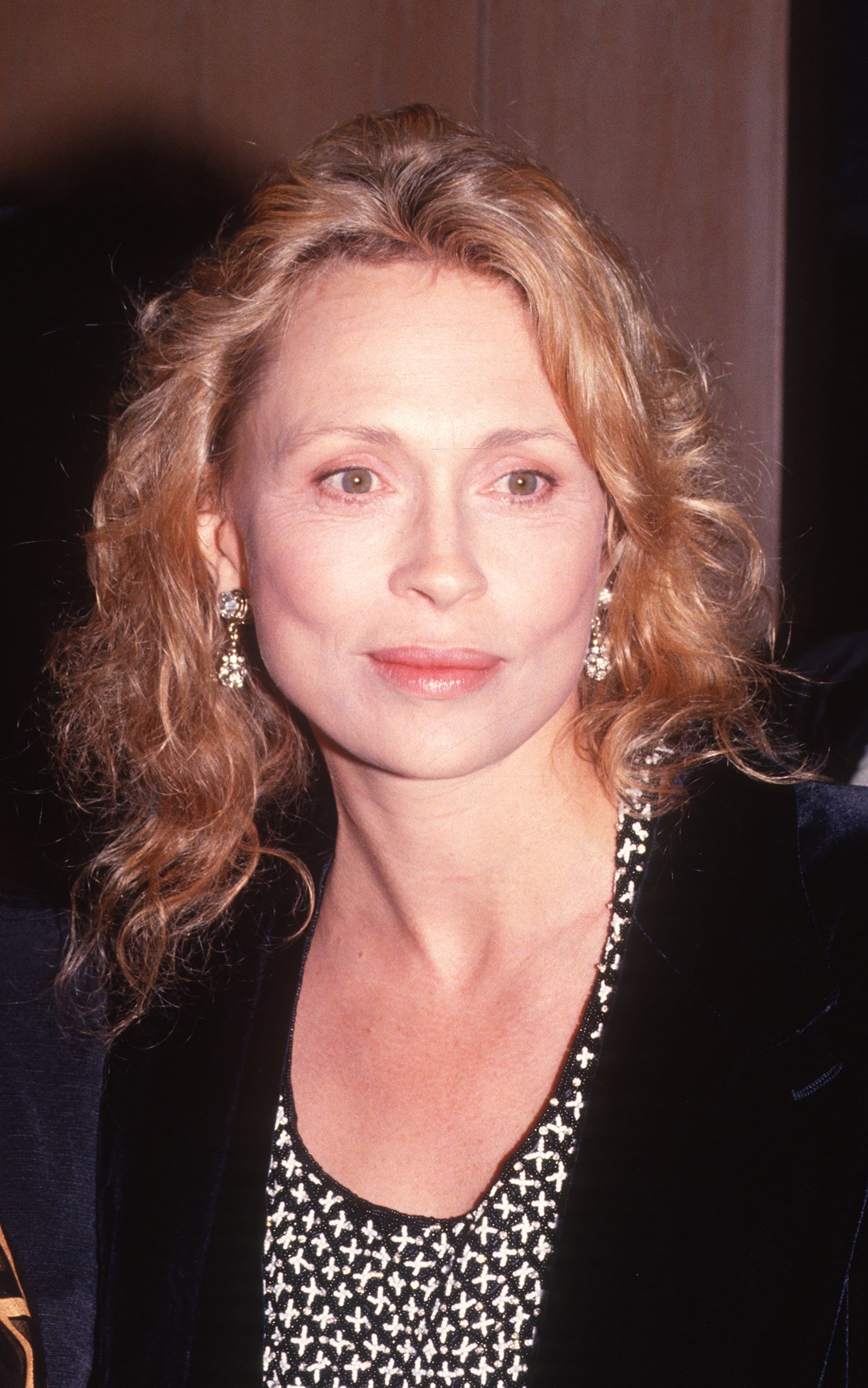 Person with wavy hair and earrings wearing a patterned top and dark blazer