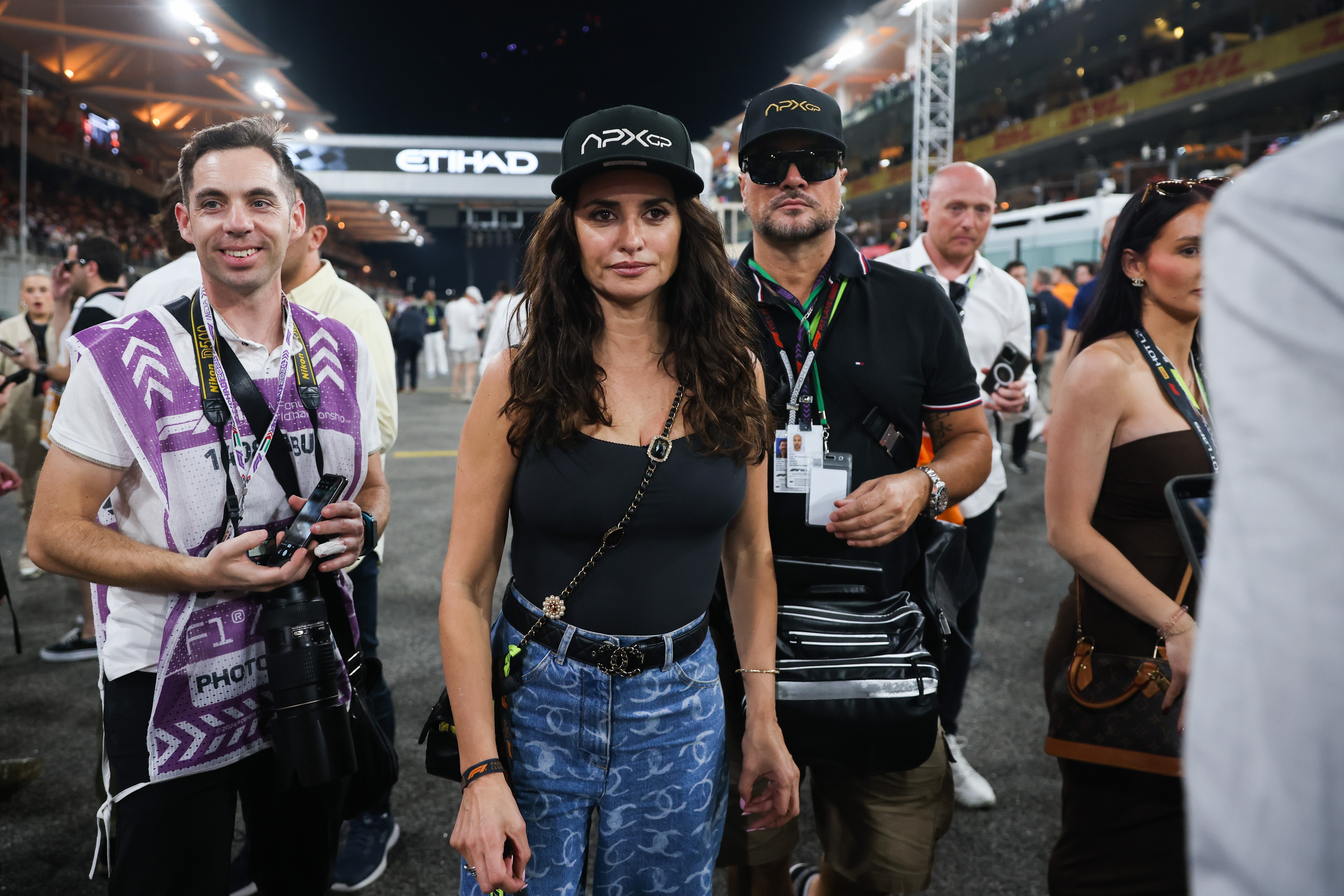 Person in casual wear and cap poses at a crowded event, photographers around