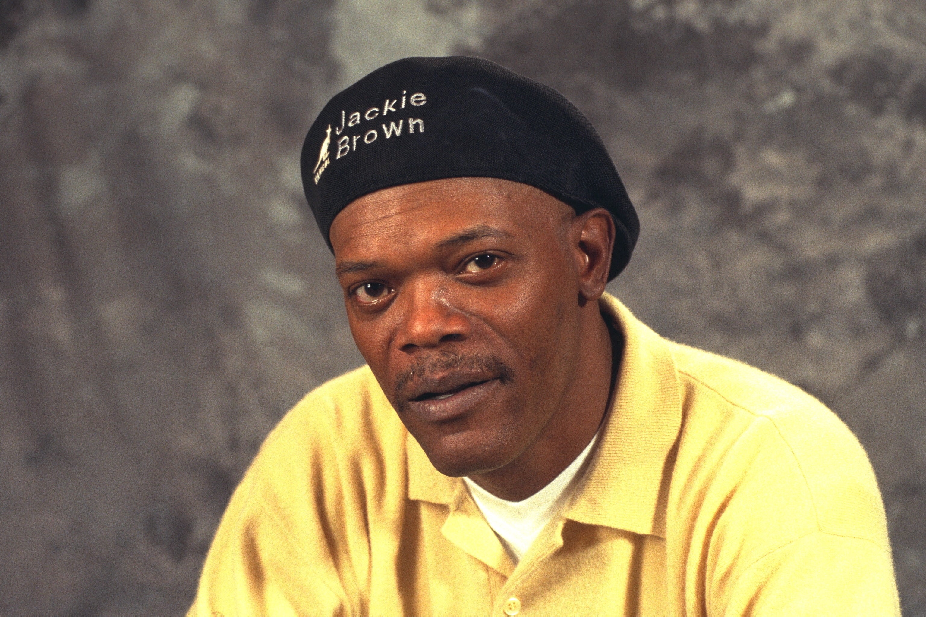 Person wearing a "Jackie Brown" beret and casual polo shirt, looking at the camera against a simple backdrop