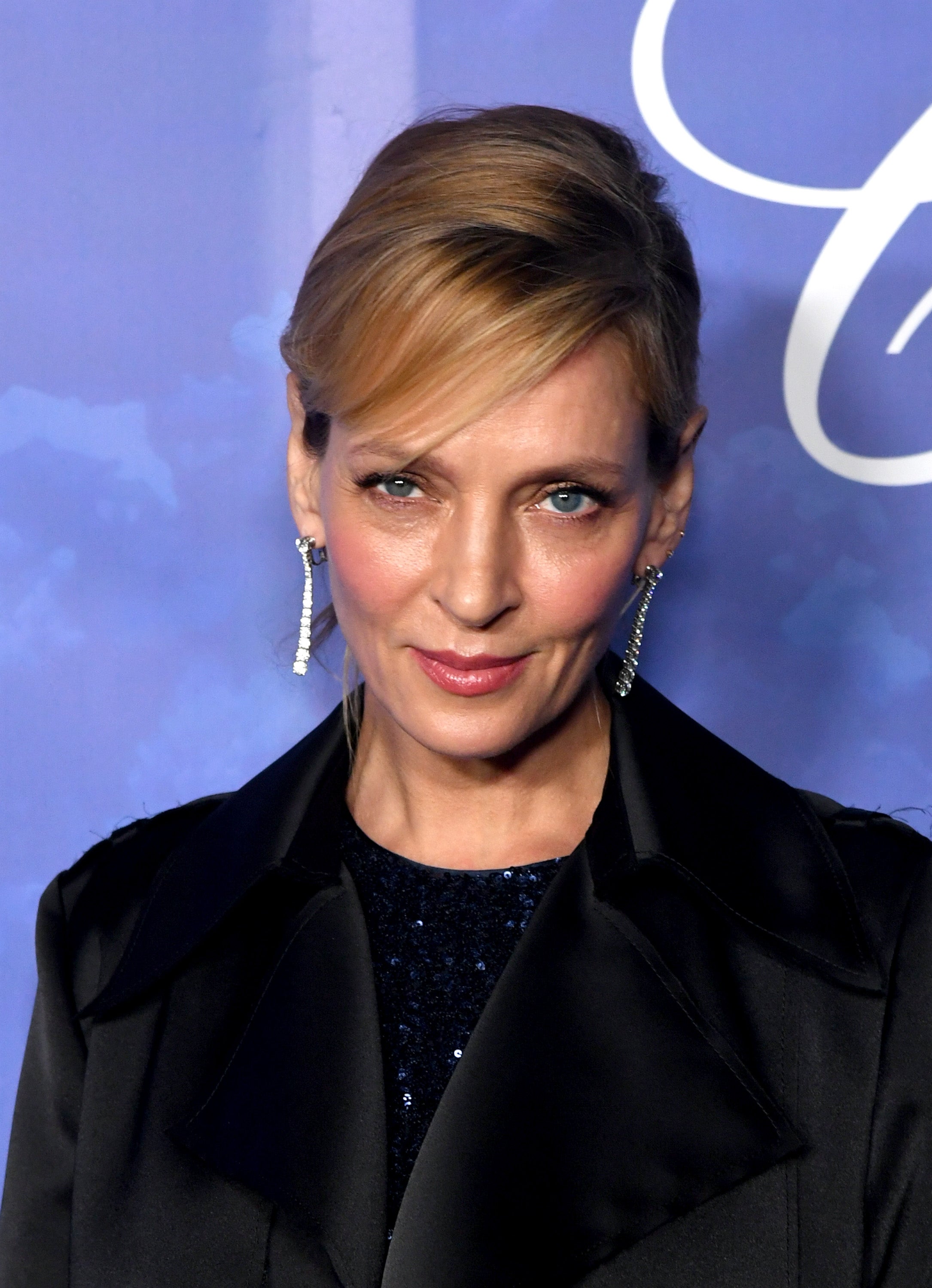 A person in an elegant black ensemble with chandelier earrings on a formal event backdrop