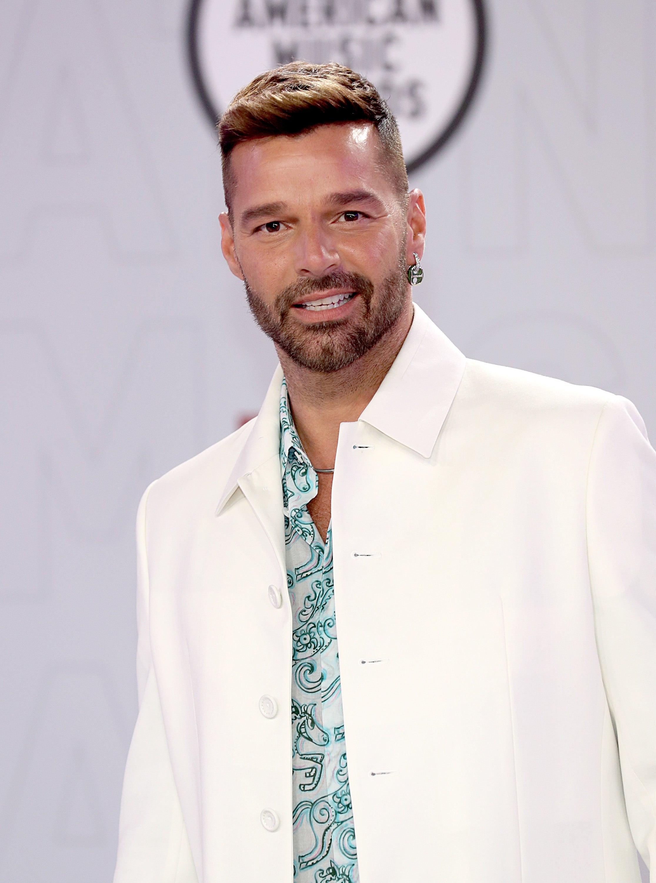 Celebrity in a stylish white jacket over a patterned shirt at a formal event, posing confidently on the red carpet