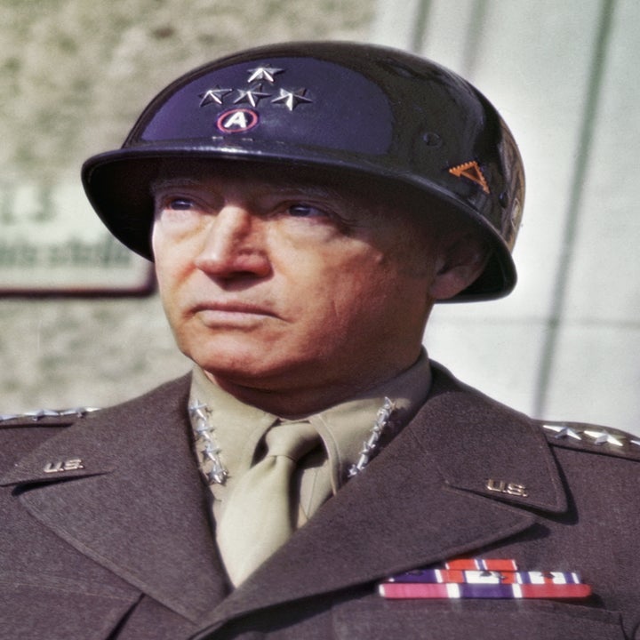 A person in a formal military uniform with decorations stands outside a building