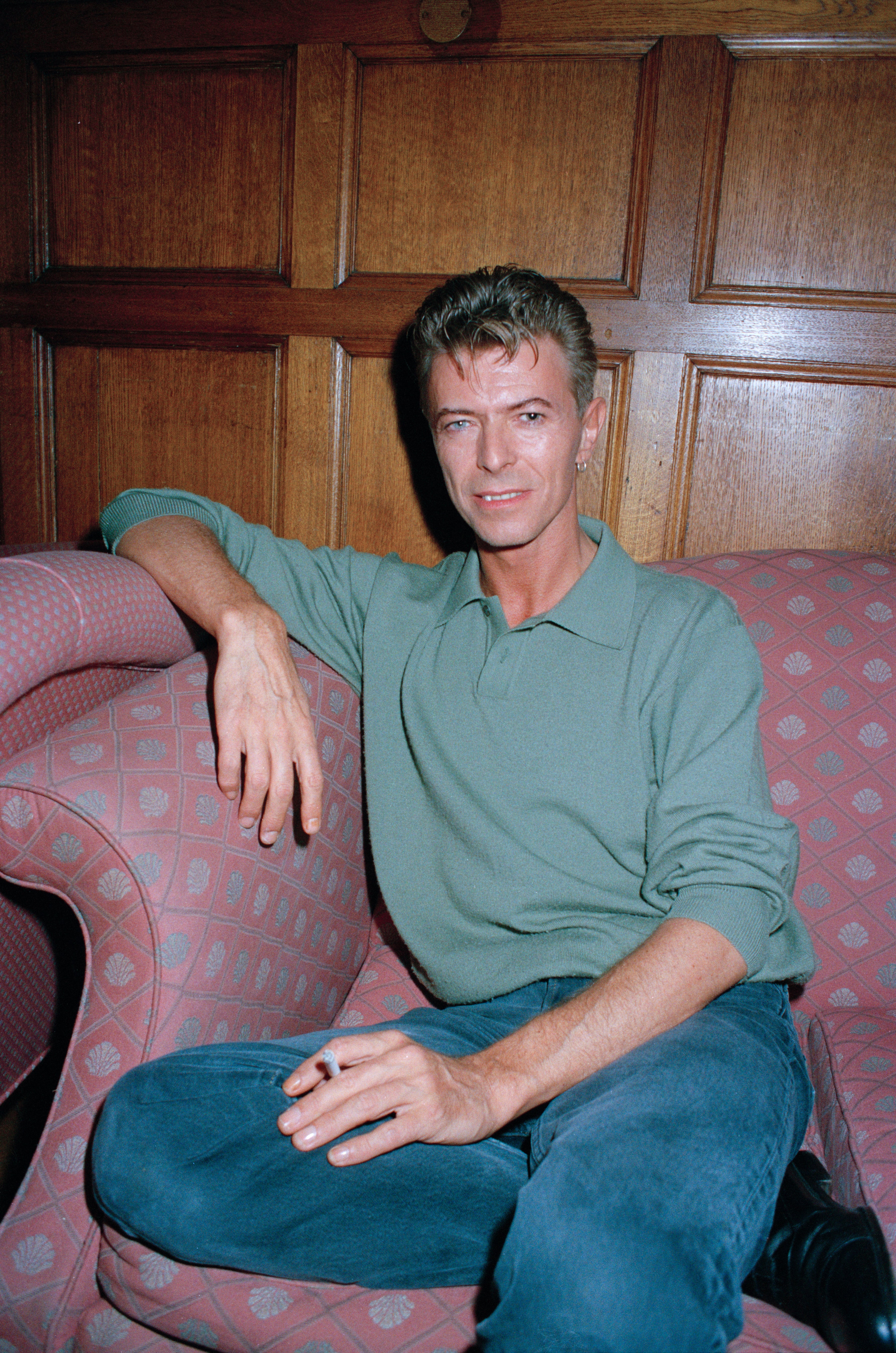 Person sitting on a patterned couch, wearing a casual collared shirt and jeans, with a relaxed expression