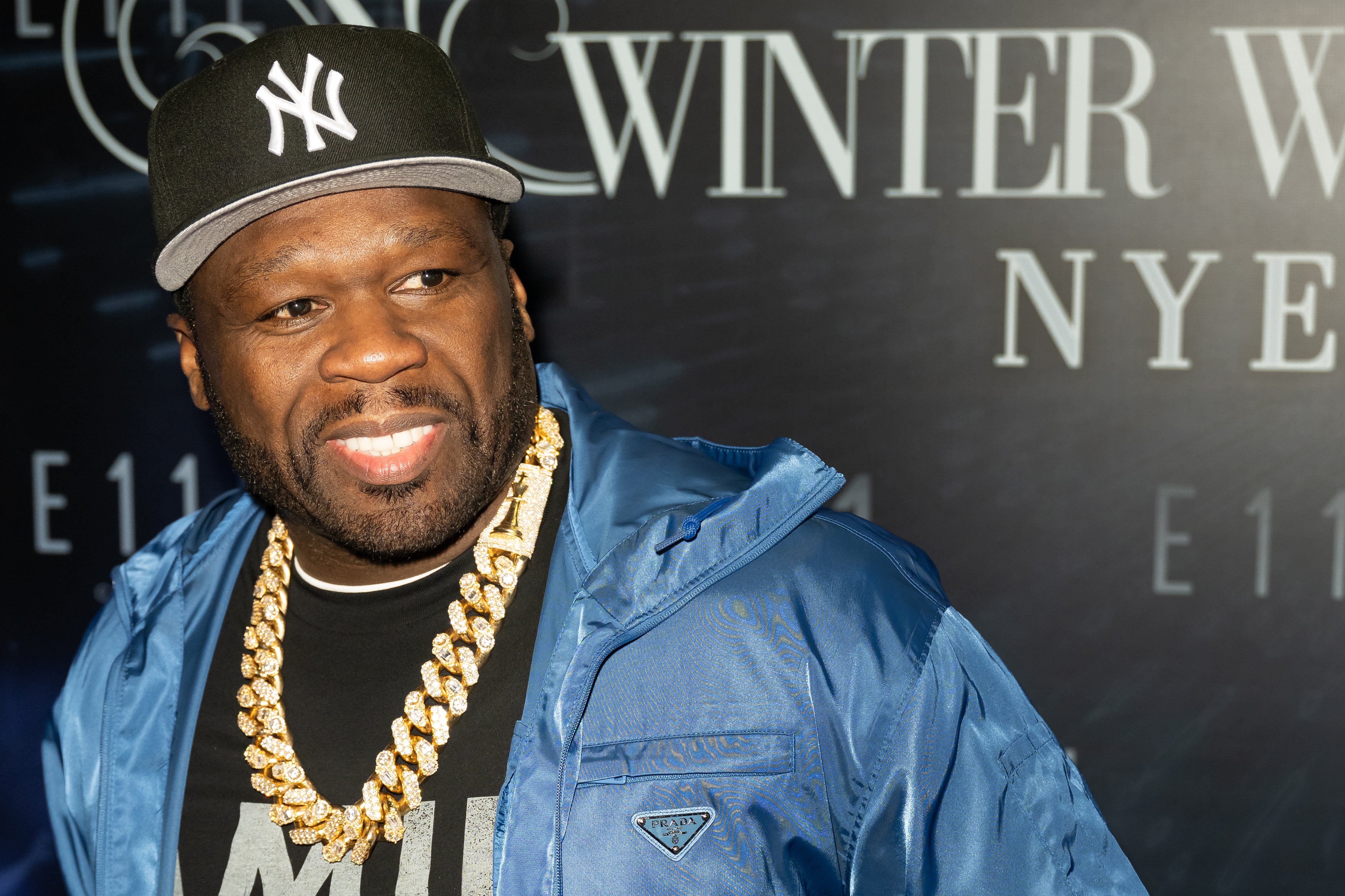 Person wearing a cap and a large chain necklace attends a winter-themed event. Background has partially visible text