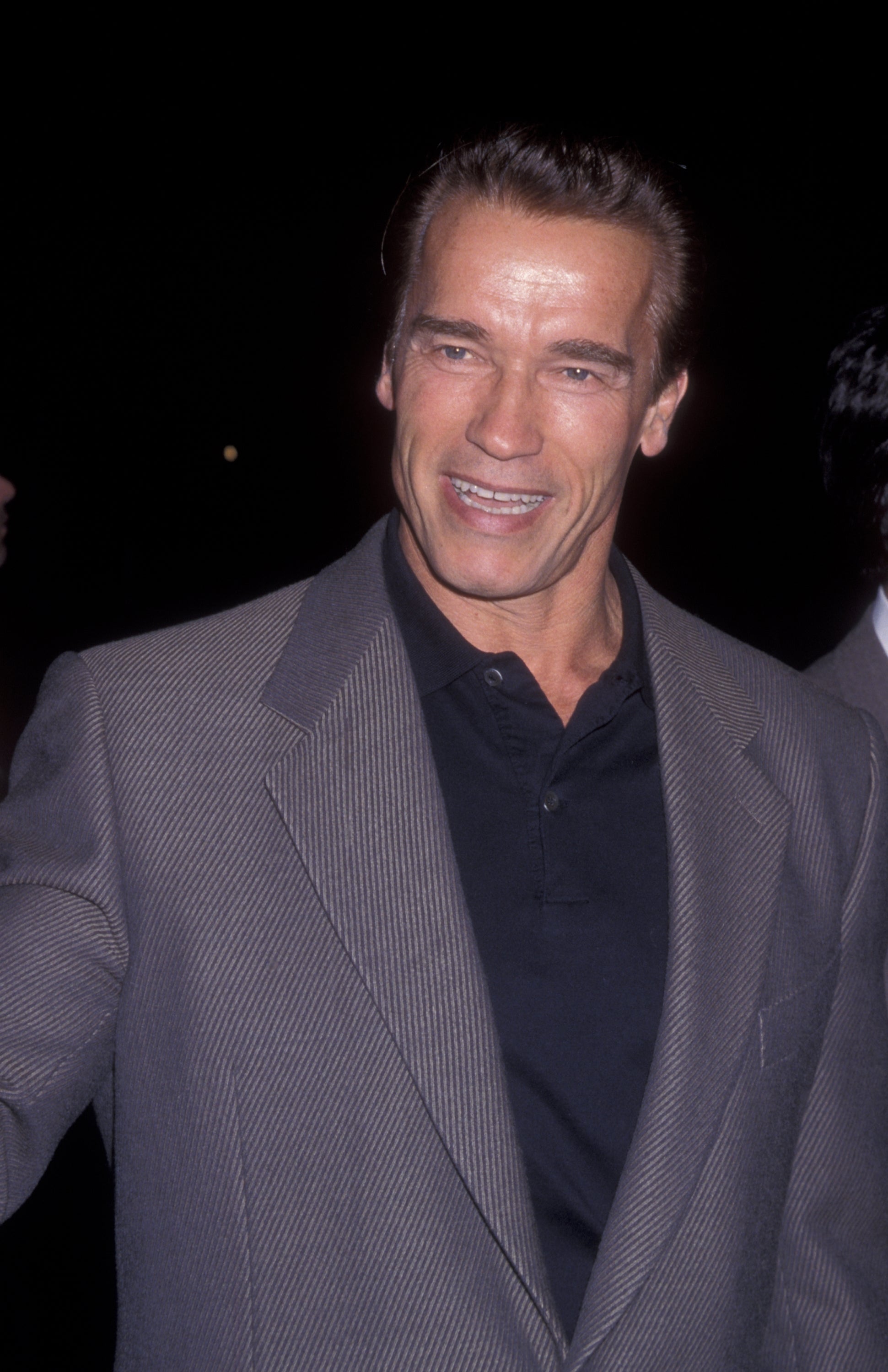 Actor in a dark shirt and striped jacket smiles at an event