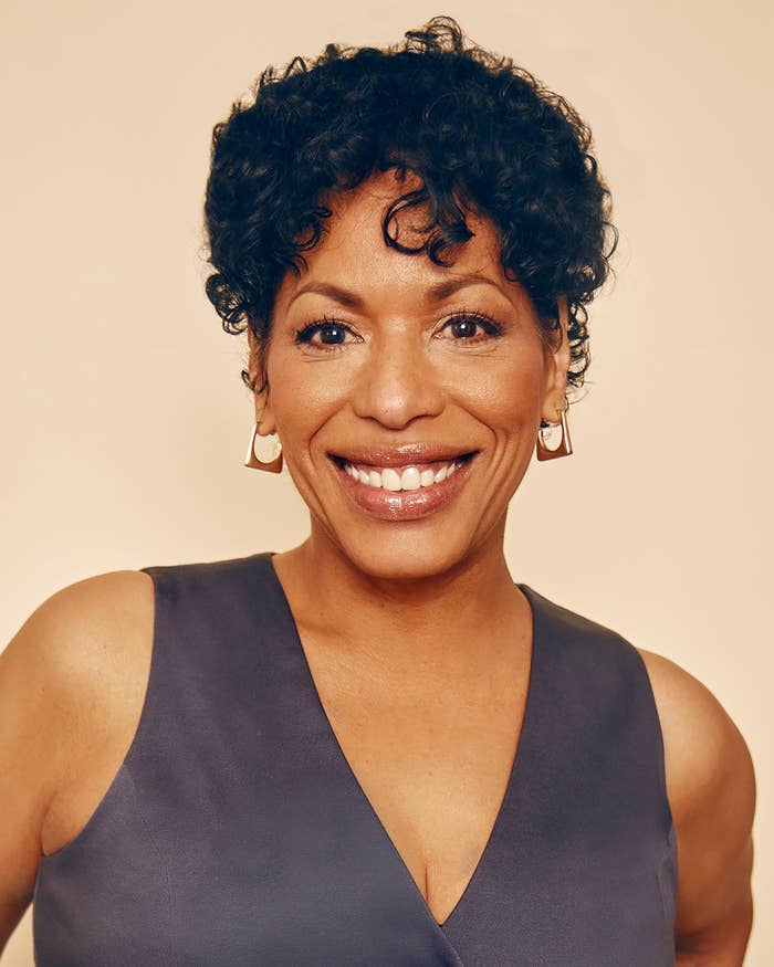 Person smiling, wearing a sleeveless V-neck top and hoop earrings