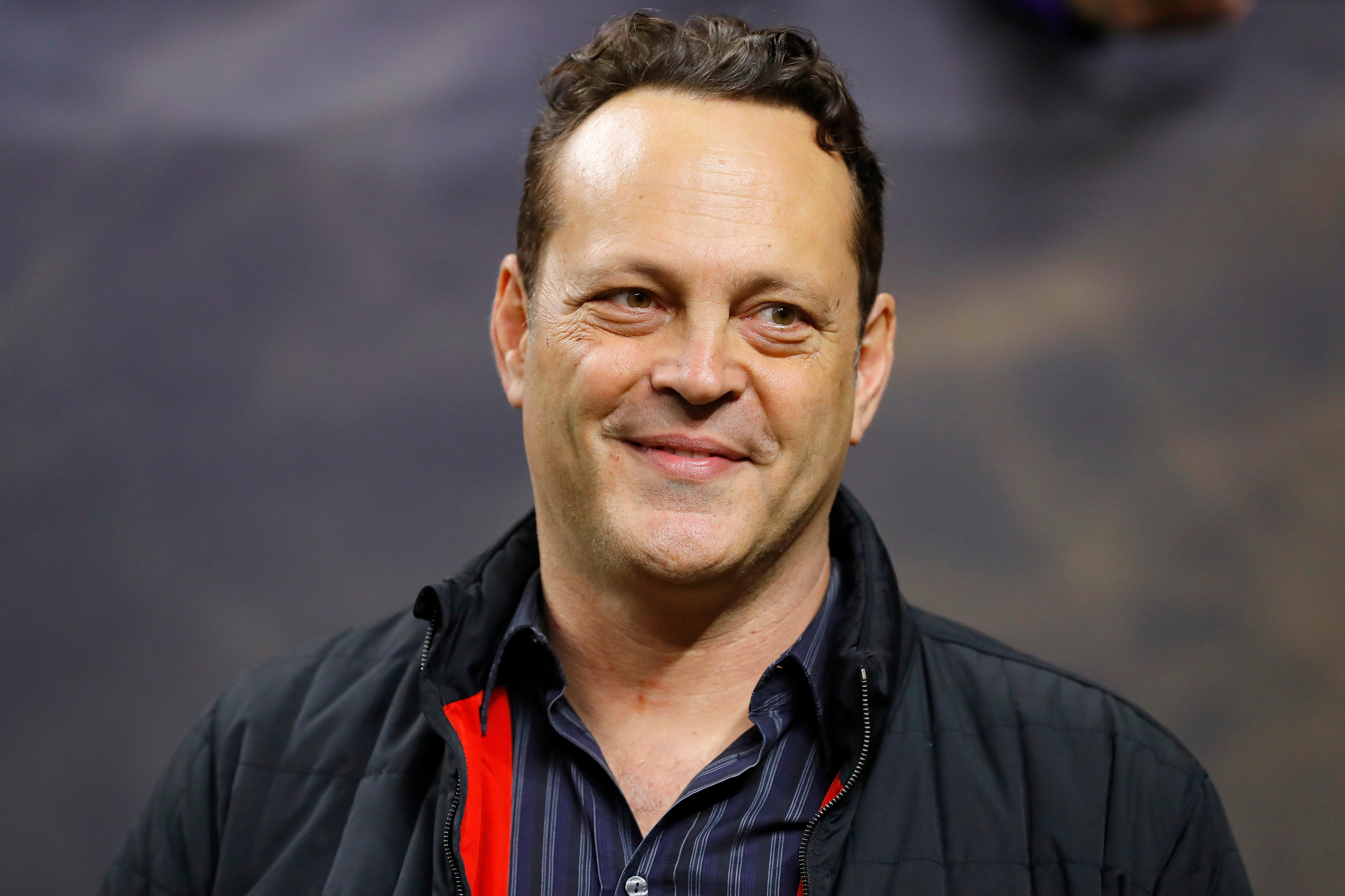 I don't know who this is, but the person smiles, wearing a dark jacket with a collared shirt underneath at a public event