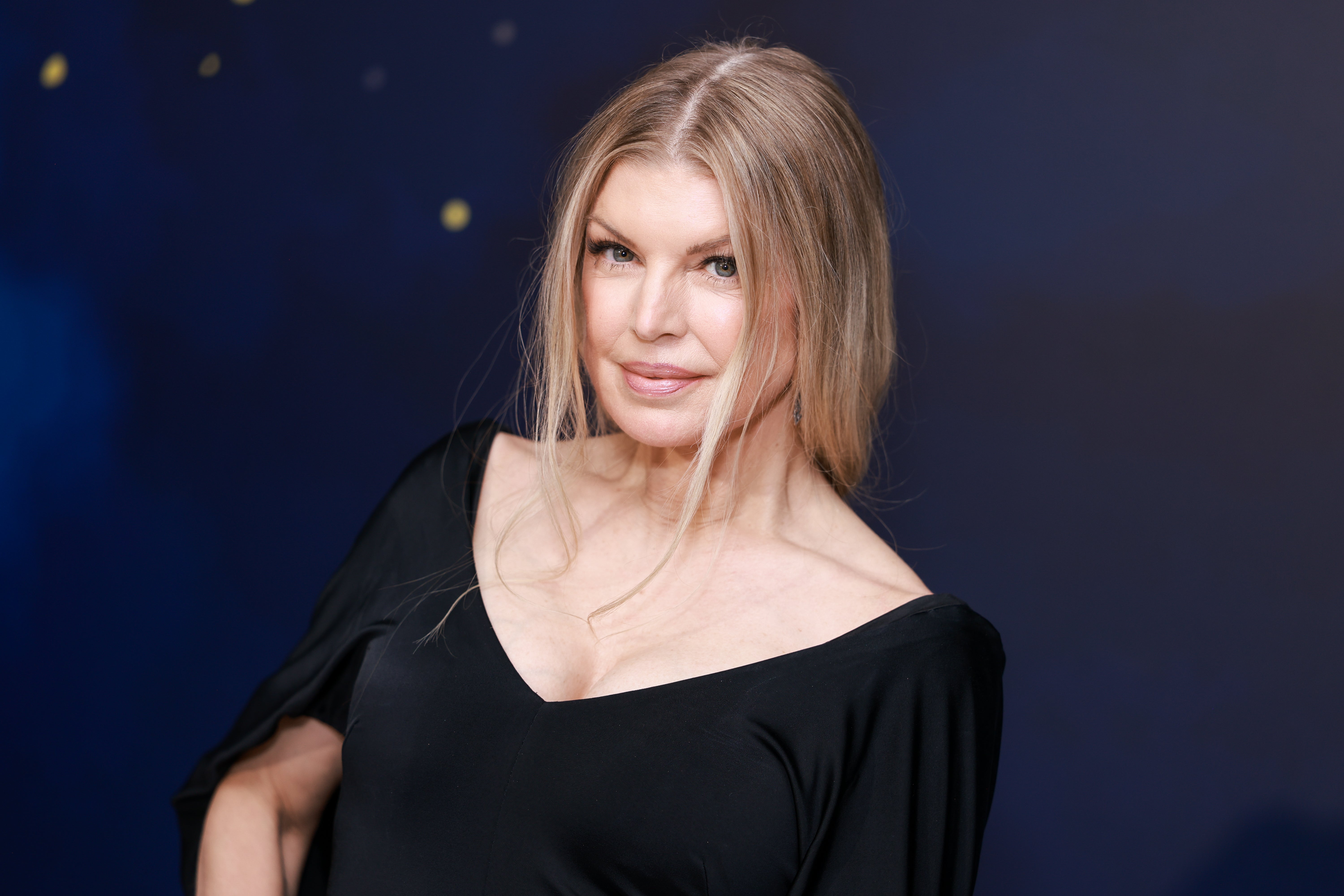Person in elegant black dress posing at an event, smiling subtly with a relaxed hairstyle