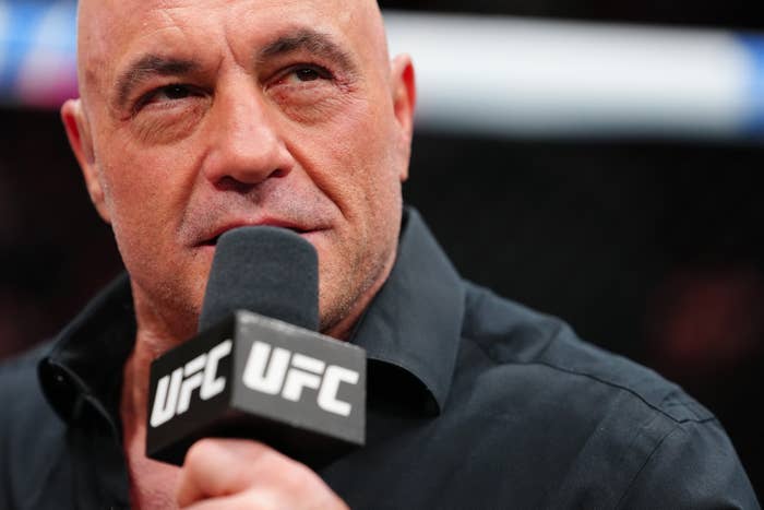 A man in a black shirt speaks into a microphone labeled "UFC" at an event
