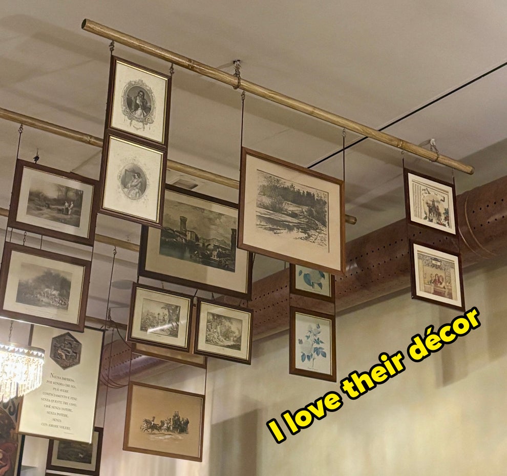 Framed photos and sketches hang from the ceiling, creating an artistic display in an indoor space reminiscent of a gallery or café