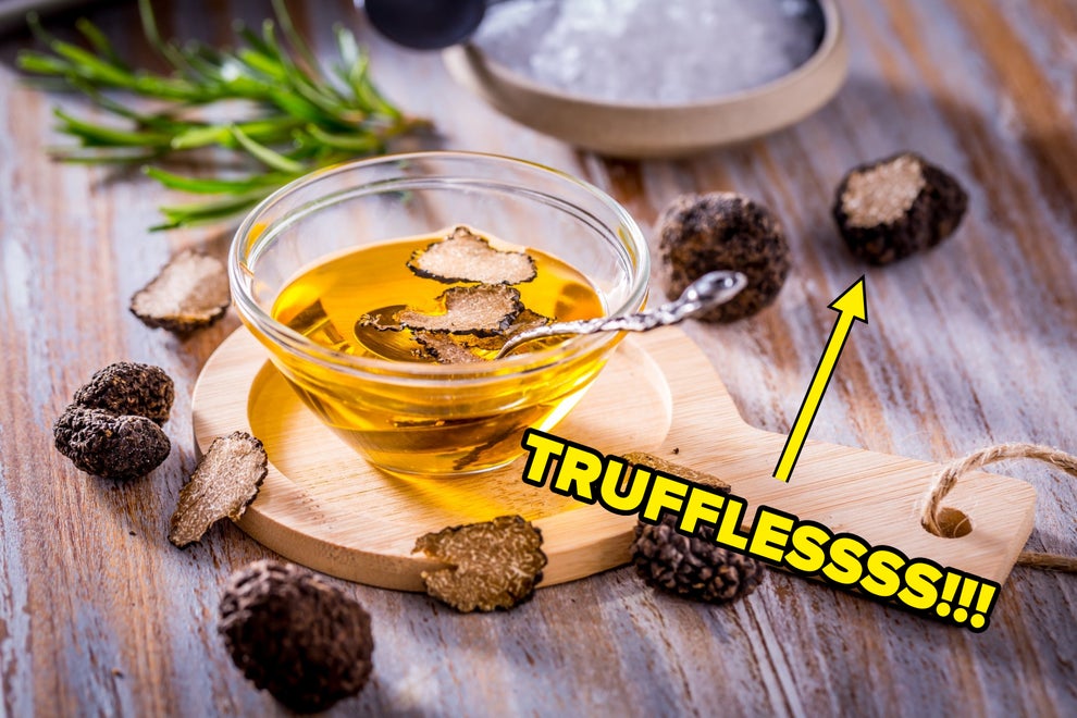 A glass bowl of truffle oil with sliced truffles and rosemary on a wooden board, surrounded by whole truffles; used in a travel-themed piece