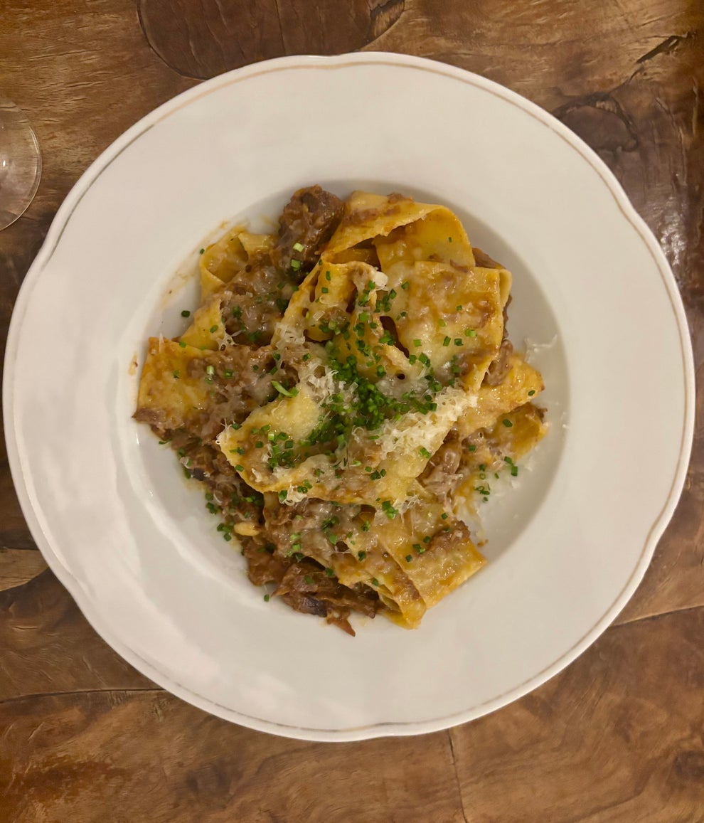 A plate of pasta with a savory meat sauce, topped with grated cheese and herbs, served on a wooden table