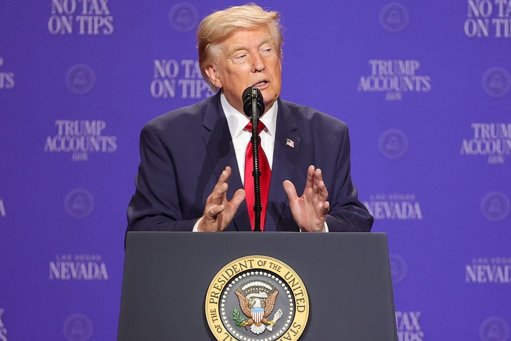 En person i dress taler ved et podium med et presidentstempel, mot et bakteppe med tekst inkludert