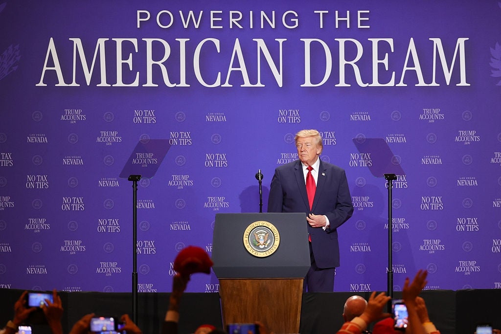 En foredragsholder på et podium med et presidentstempel, som henvender seg til et publikum. Bak, en stor "Powering the American Dream" banner vises