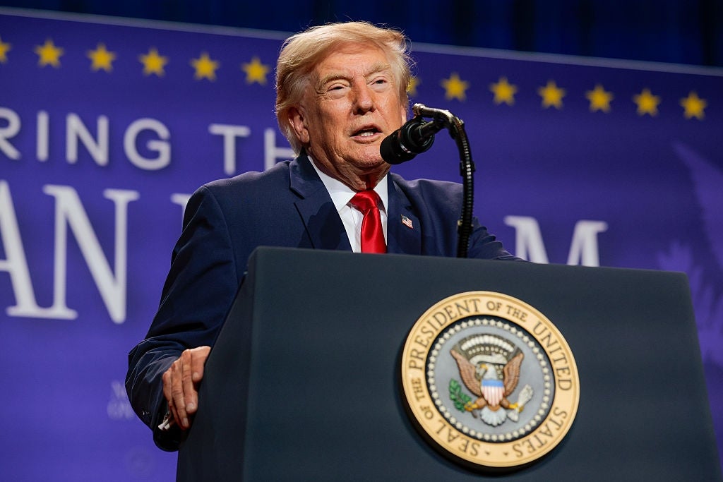 En person som snakker på et podium med seglet til presidenten i USA, på et arrangement med et banner i bakgrunnen