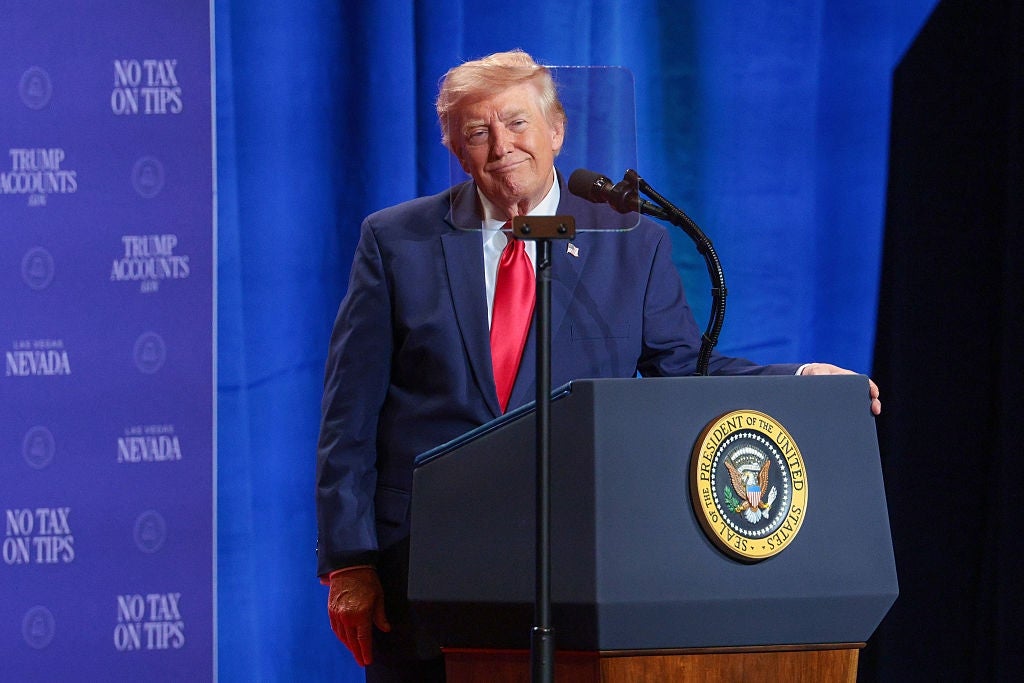 Person i dress som snakker på et podium med en mikrofon og en presidentsegl, foran et bakteppe med gjentatt tekst om skatter og Nevada
