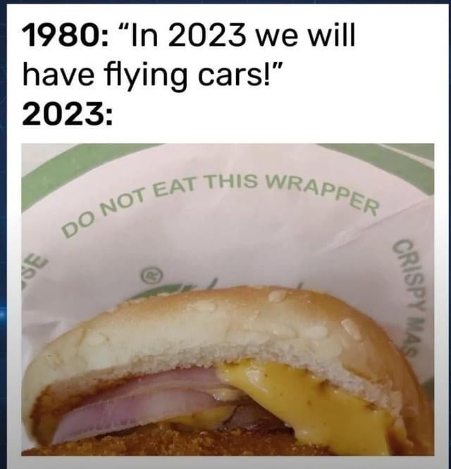 Burger half-wrapped in paper labeled "DO NOT EAT THIS WRAPPER," humorously contrasting 1980's flying car prediction with 2023's reality