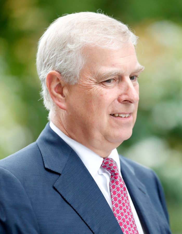 An older man in a suit with a patterned tie is outdoors, smiling slightly