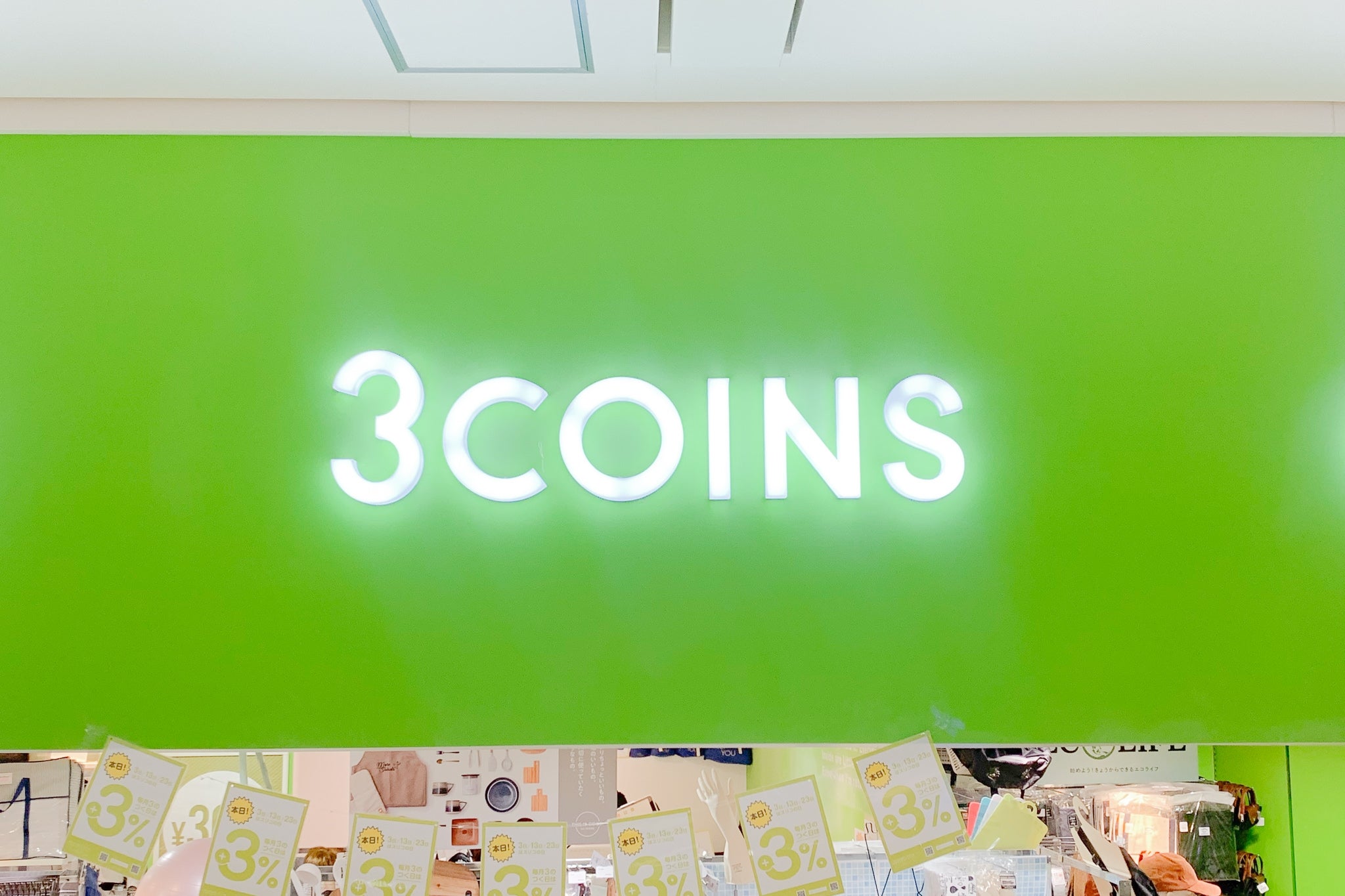 緑色の背景に「3COINS」のロゴが光っている。下には3%オフのチラシが並んでいる。