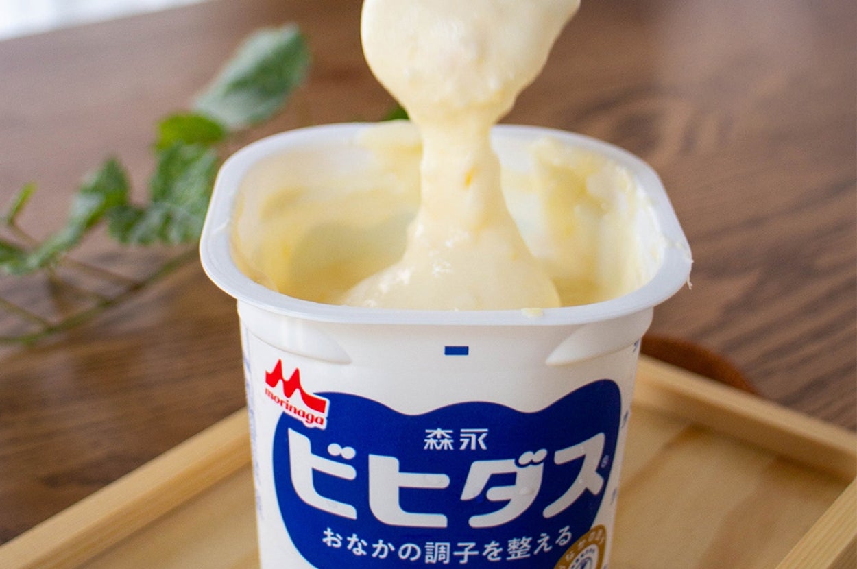 森永ビヒダスプレーンヨーグルトがスプーンからすくわれている様子。テーブルに置かれたヨーグルト容器。