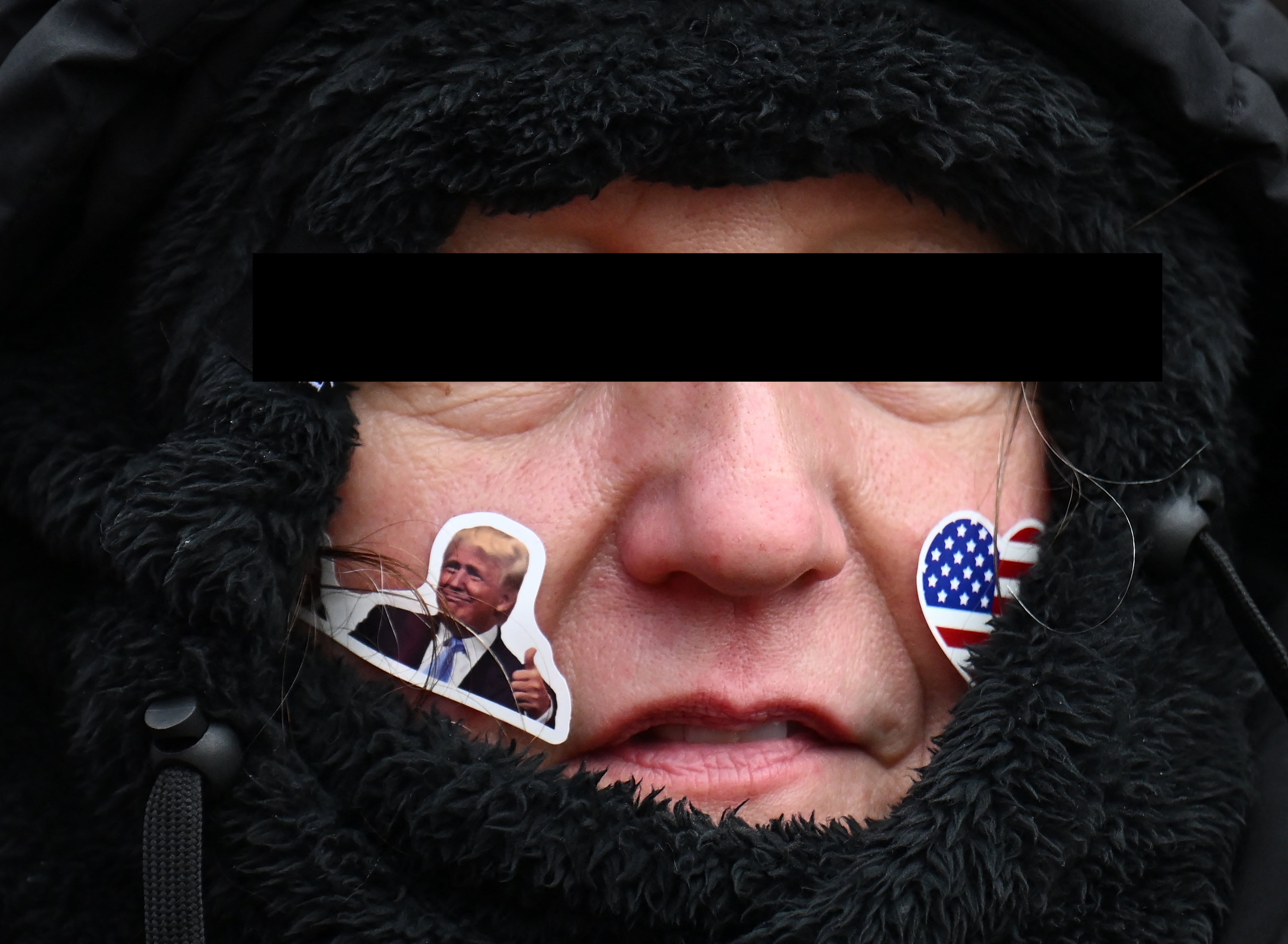 Person som har på seg en svart hette med Trump og amerikansk flaggklistremerker i ansiktet, ser alvorlig ut
