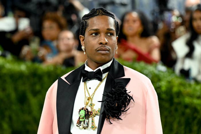 Person in a tuxedo with ornate accessories on a formal event carpet, surrounded by attendees