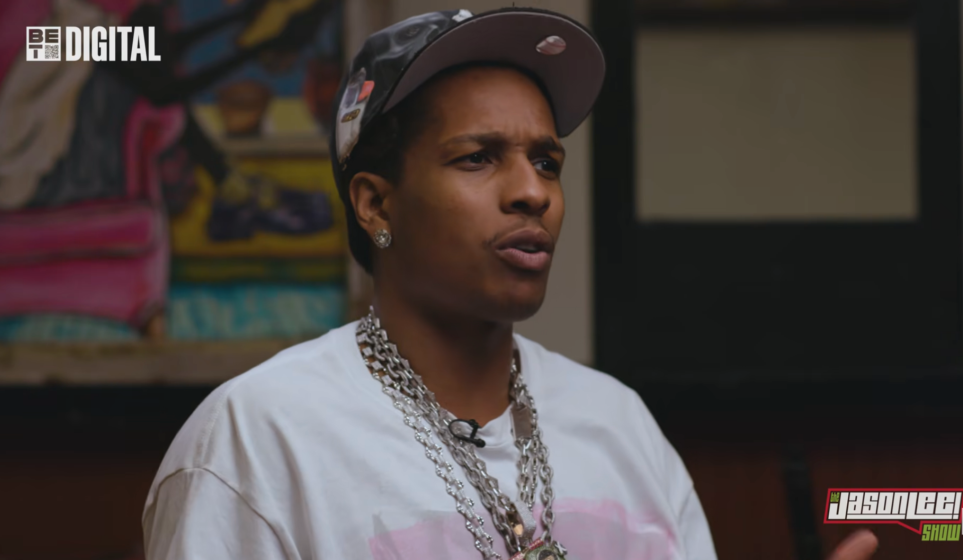 Person in a casual shirt, cap, and chain speaking during an interview. Logos of BET Digital and Jason Lee Show visible