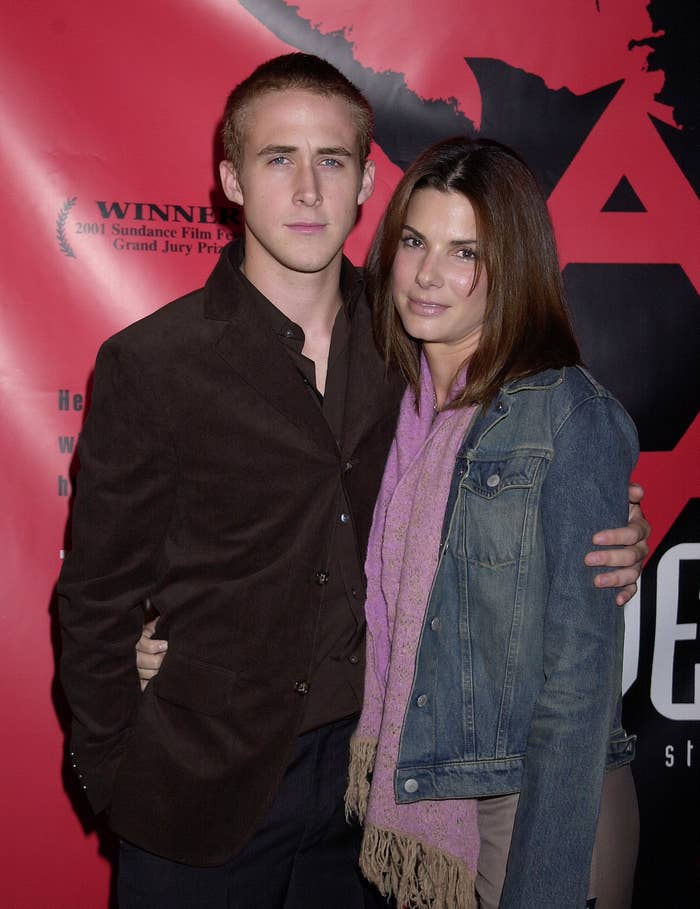 Two people posing together at an event. One wears a blazer and shirt, the other a denim jacket and scarf