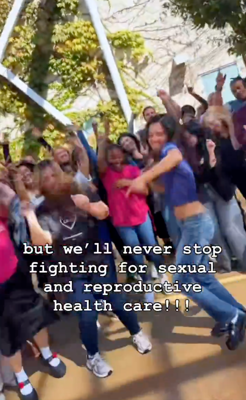 Group of people celebrating outdoors, some jumping. Text: "but we'll never stop fighting for sexual and reproductive health care!!!"