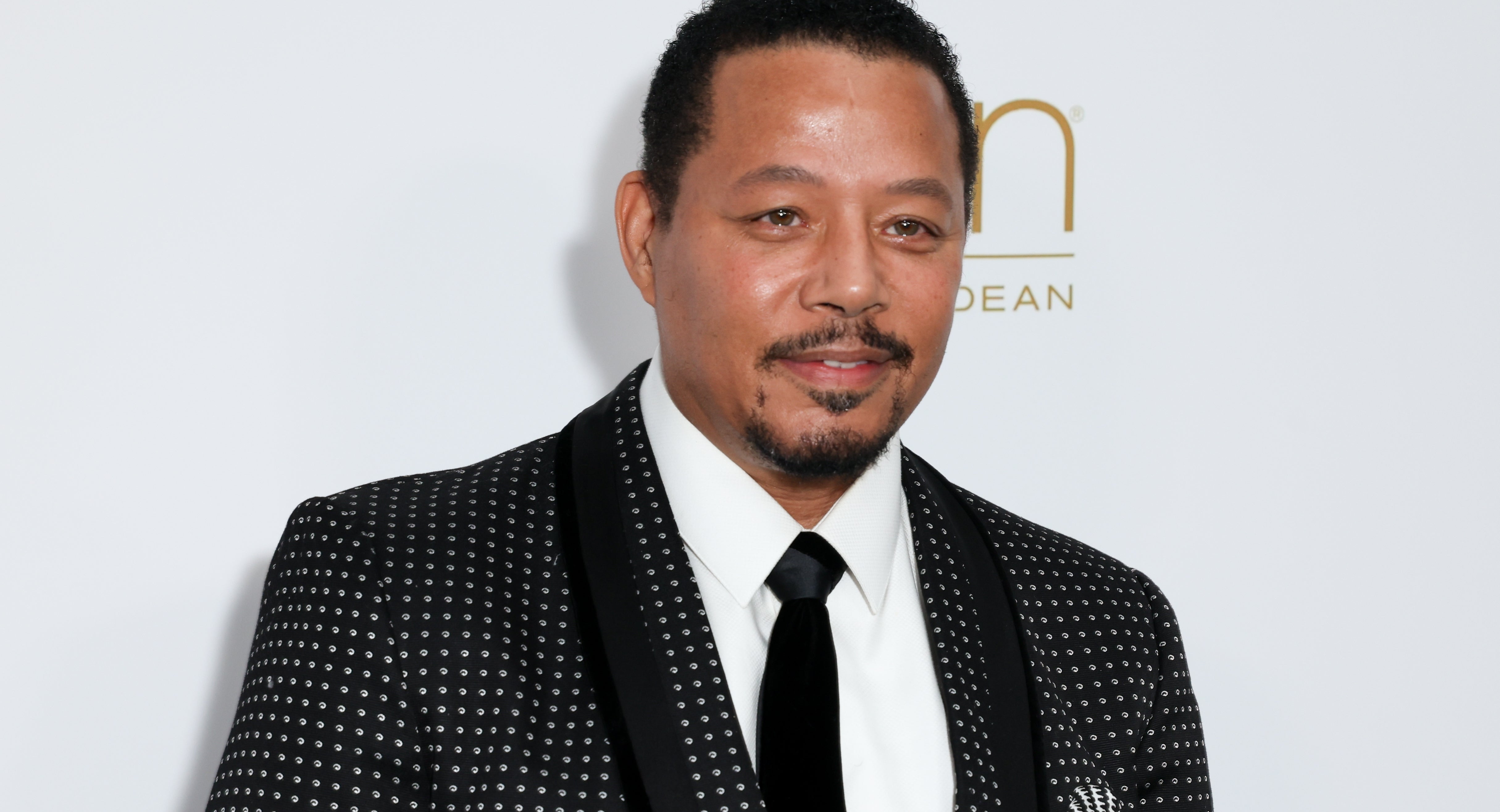 A person in a patterned suit with a black tie poses at a formal event