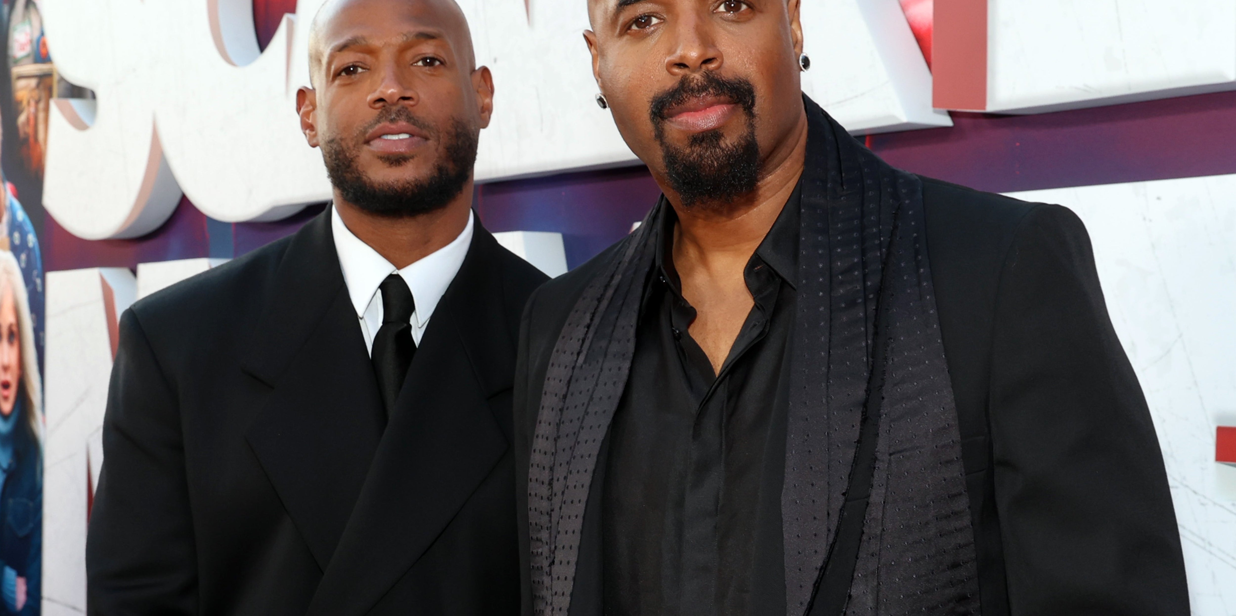 Two celebrities at a red carpet event, both wearing dark suits and shirts