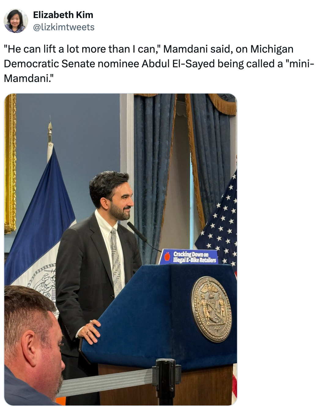 Person på podiet, snakker i en formell setting med gardiner, bildeteksten diskuterer Abdul El-Sayed som humoristisk blir kalt en