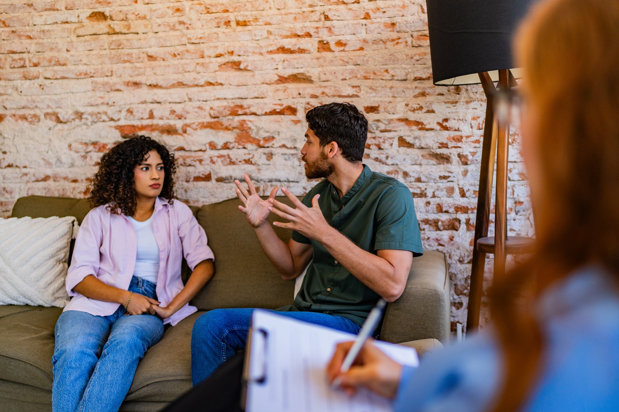 A couple is in a counseling session, appearing to be in a serious discussion while a therapist takes notes