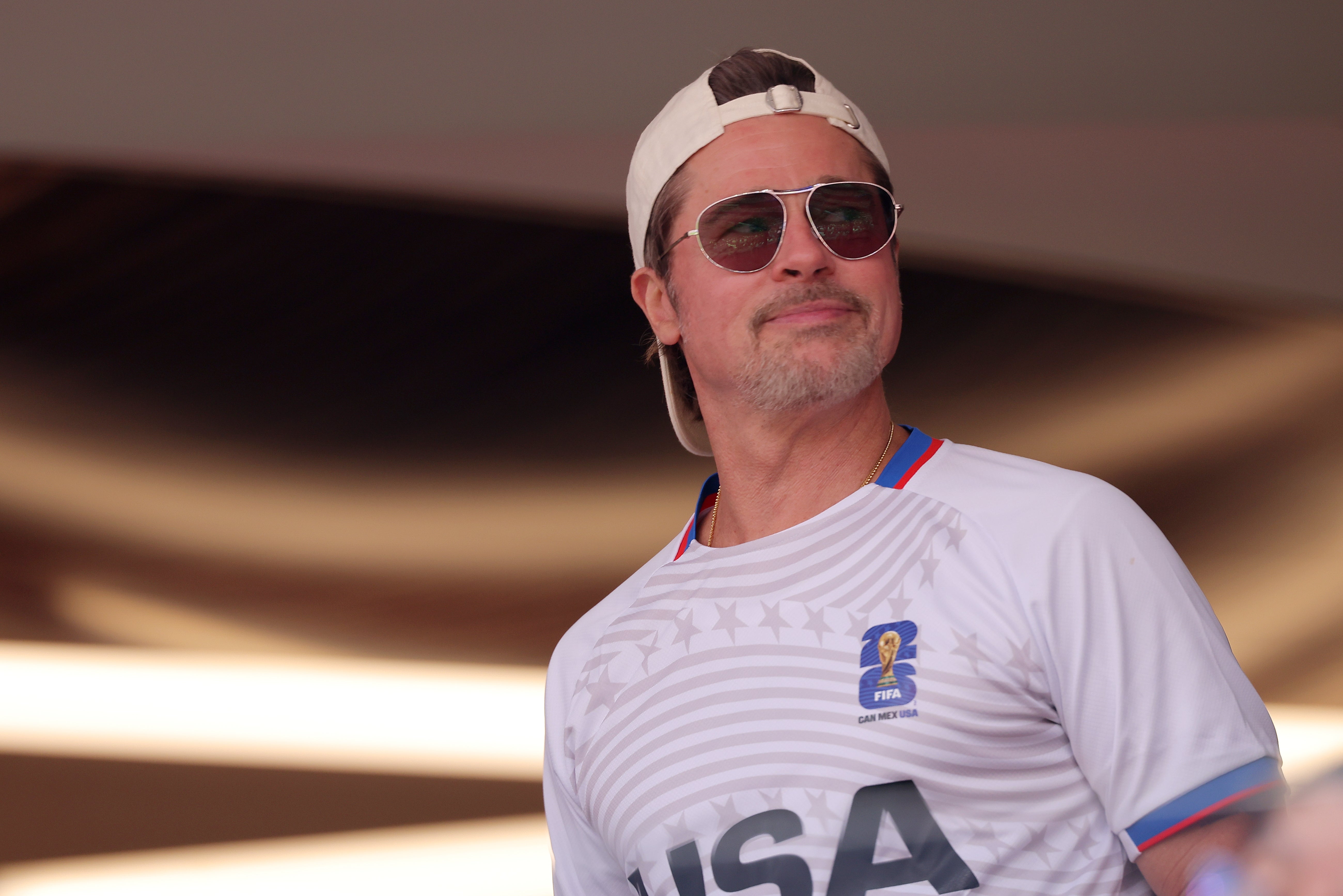 Person in a casual white sports jersey, cap, and sunglasses, smiling in a relaxed pose