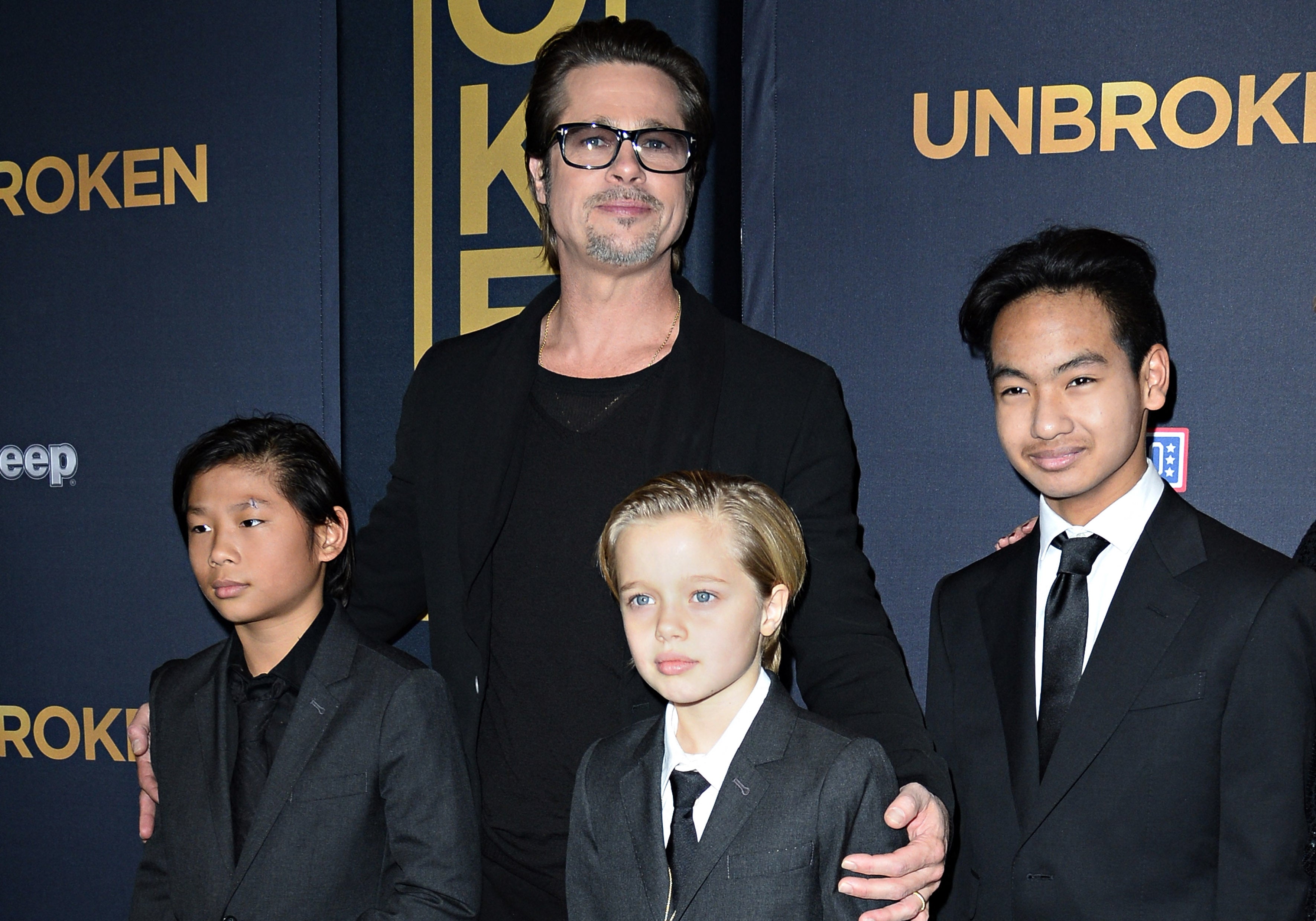 A person in a black suit stands with three children in suits at a movie premiere