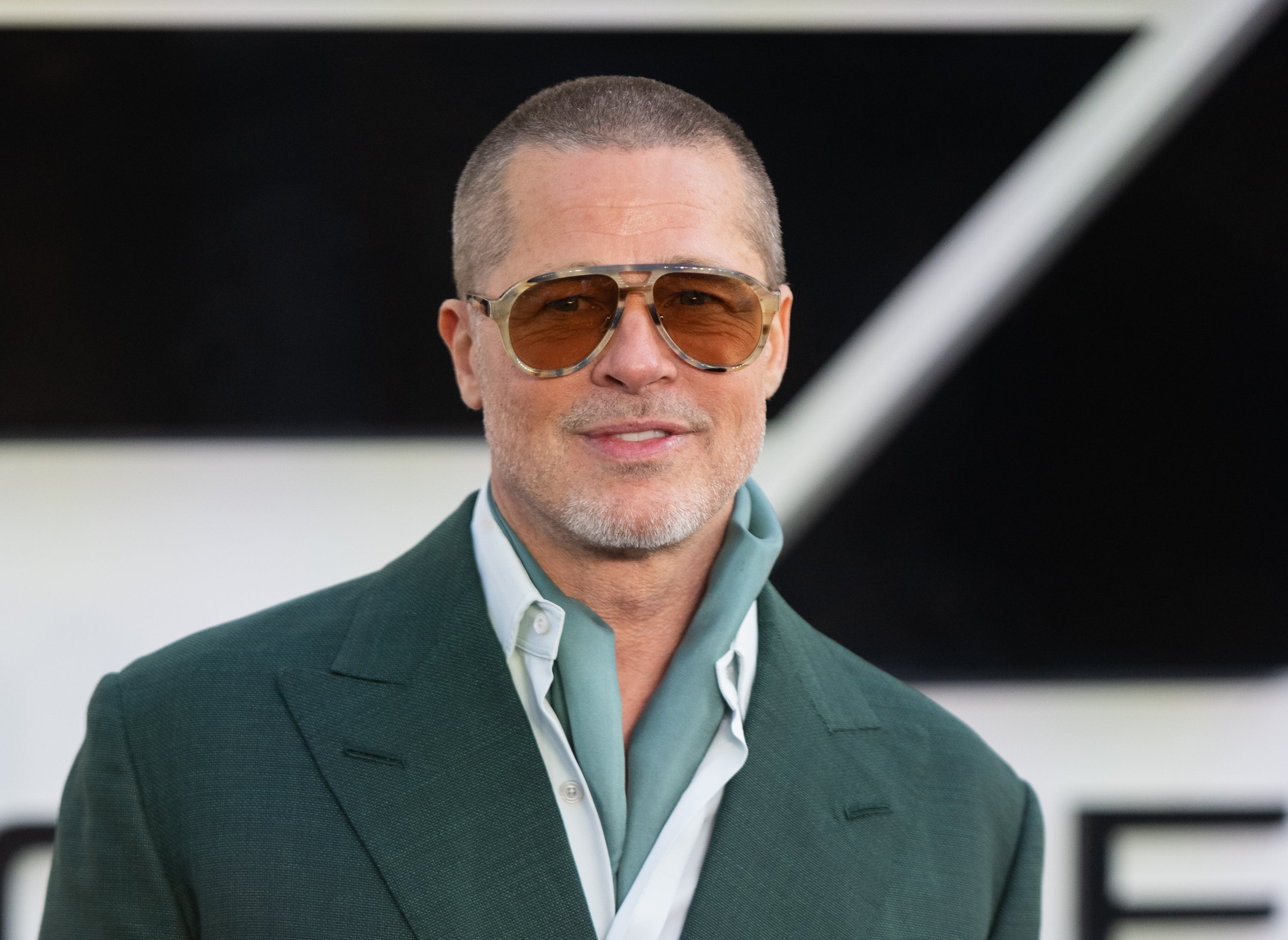 Person in sunglasses and green suit with relaxed collar, smiling at an event
