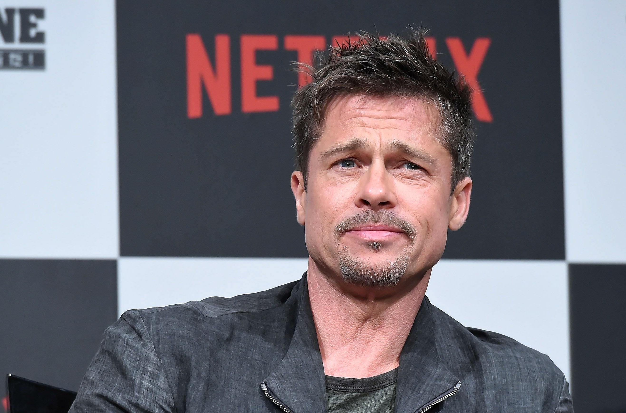 A man in a casual jacket sits during a Netflix event, posing mid-sentence with an inquisitive expression. Netflix logo visible in the background