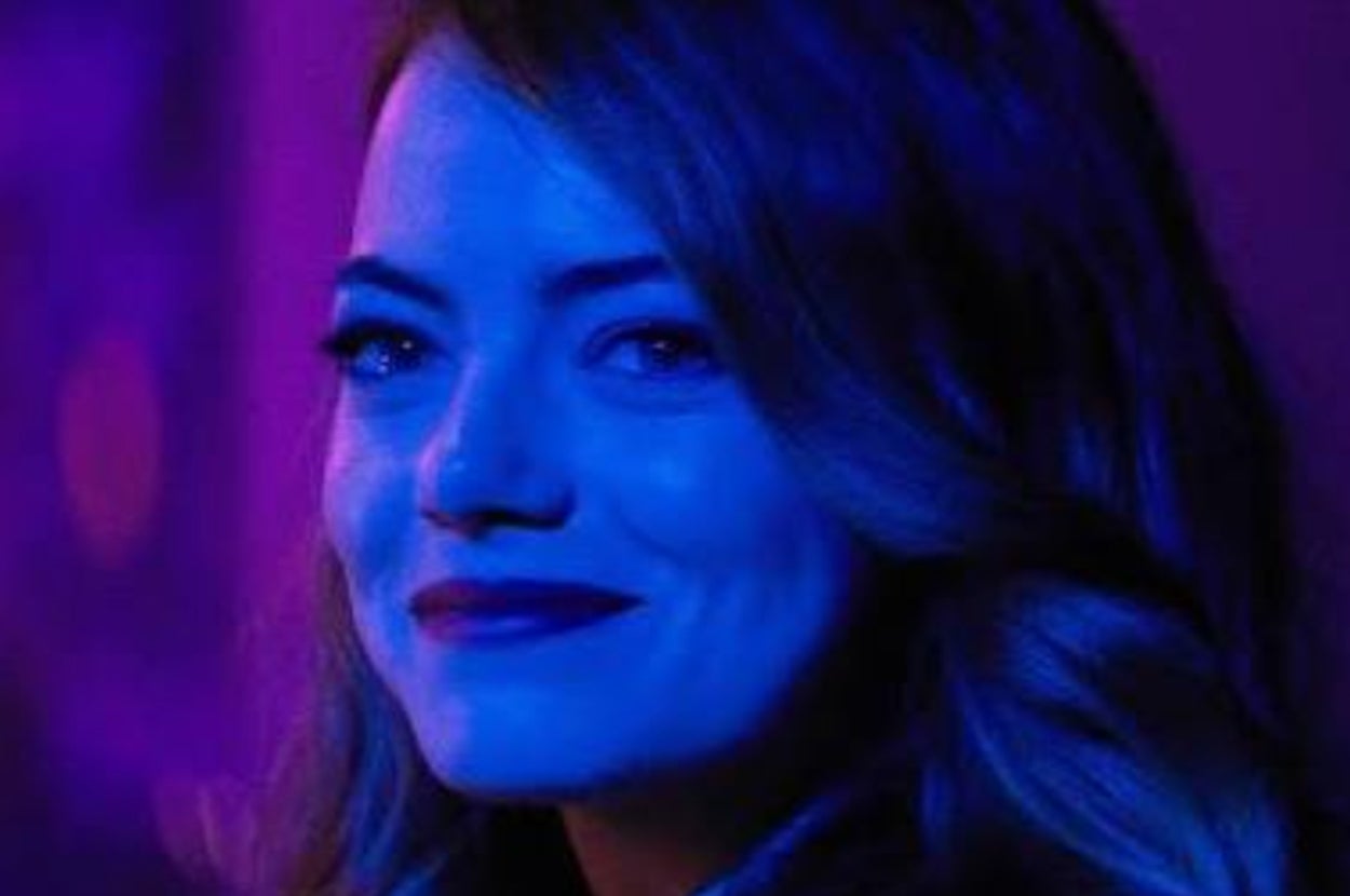 A person with long hair smiling softly under dramatic blue lighting