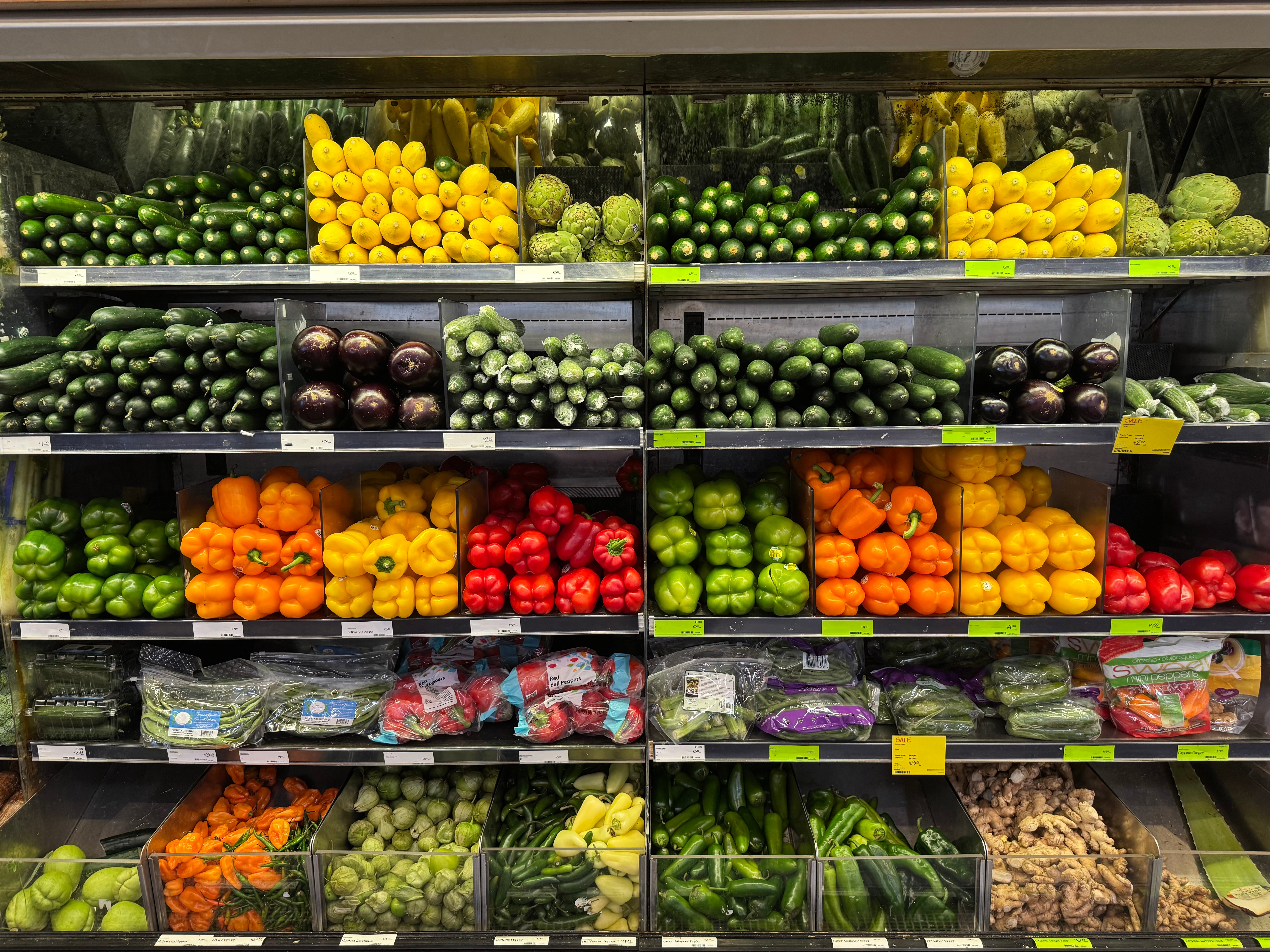 Supermarked produsere seksjon med en rekke grønnsaker, inkludert paprika, agurker og auberginer, pent arrangert i hyllene