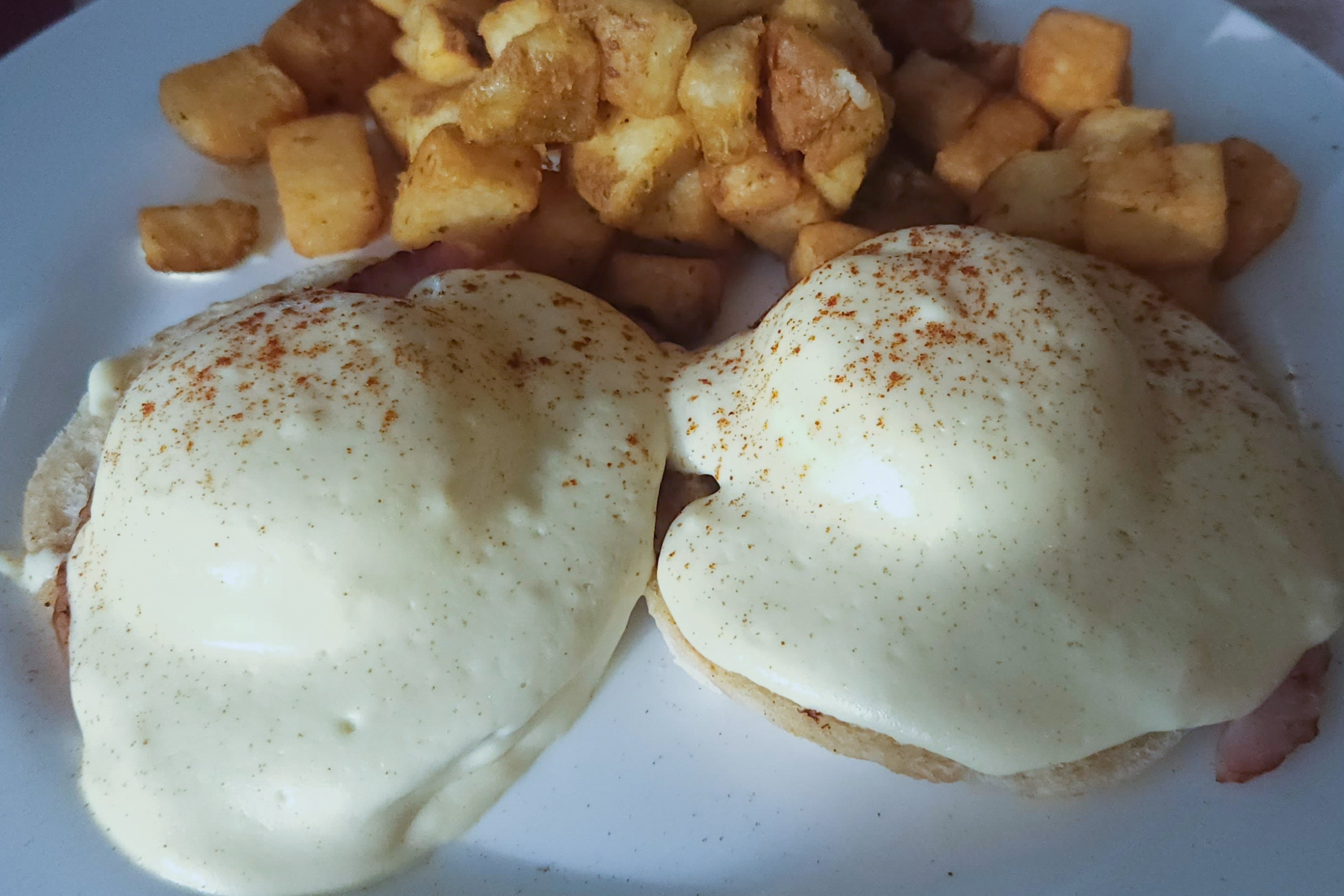 Eggs Benedict med hollandaisesaus og paprika, servert sammen med krydrede poteter i terninger på tallerken