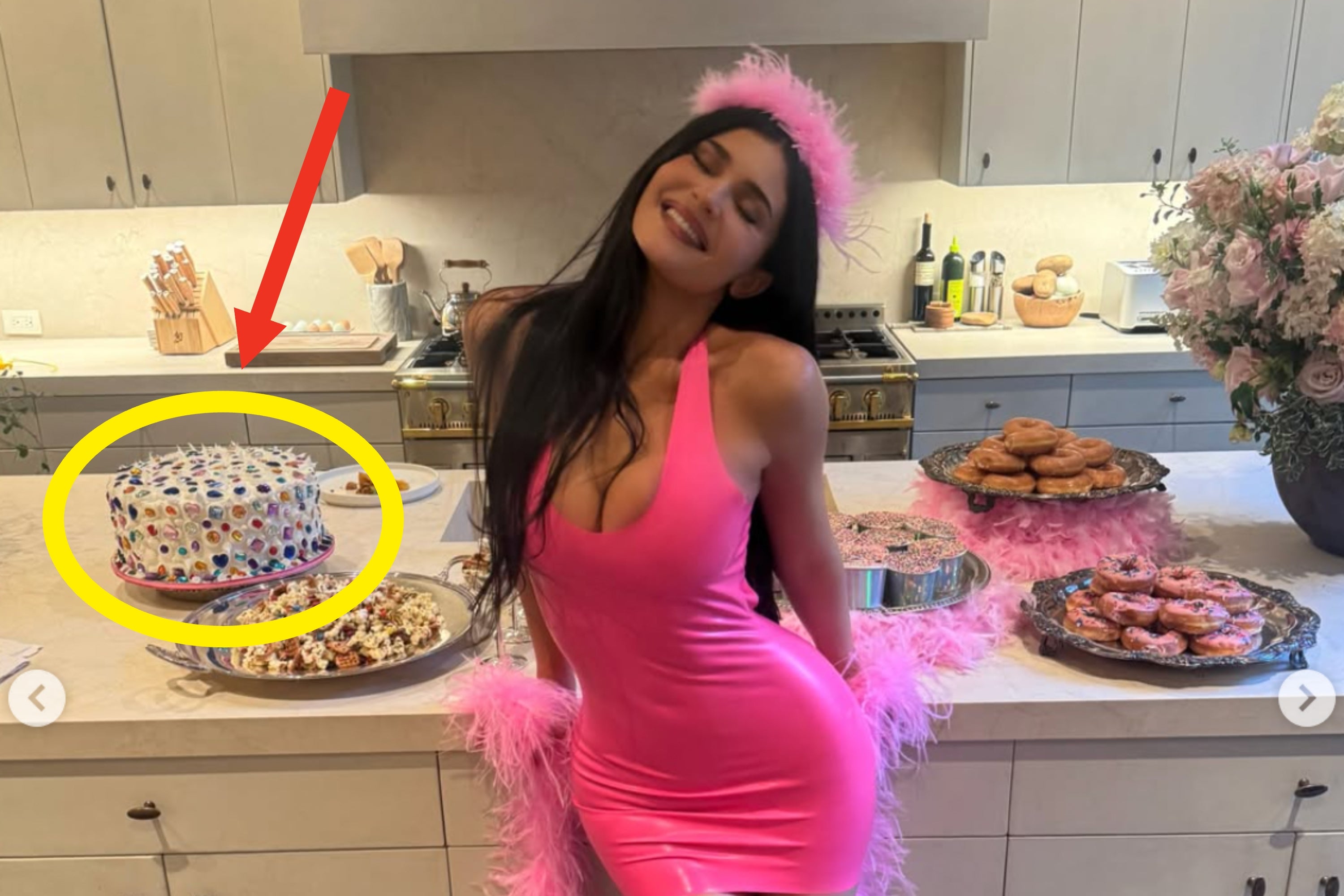 Person in a fitted dress and feathered accessories poses playfully in a kitchen with assorted food dishes on display