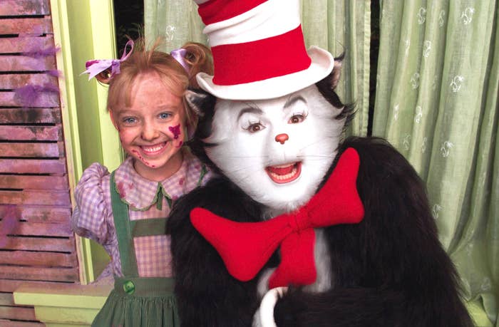 Child posing with a person in a Cat in the Hat costume, featuring a large red bow tie and signature striped top hat