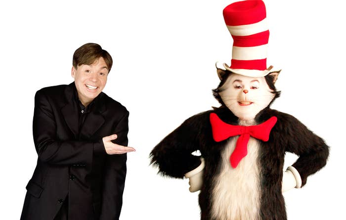 Person in a suit smiling and pointing at someone dressed as the Cat in the Hat, wearing a large red and white striped hat and red bow tie