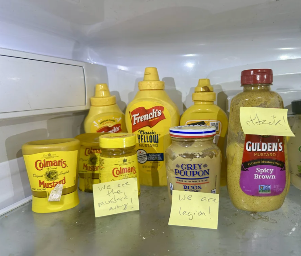 Refrigerator shelf filled with various mustard containers. Two sticky notes read, "We are mustard army!" and "We are legion!"