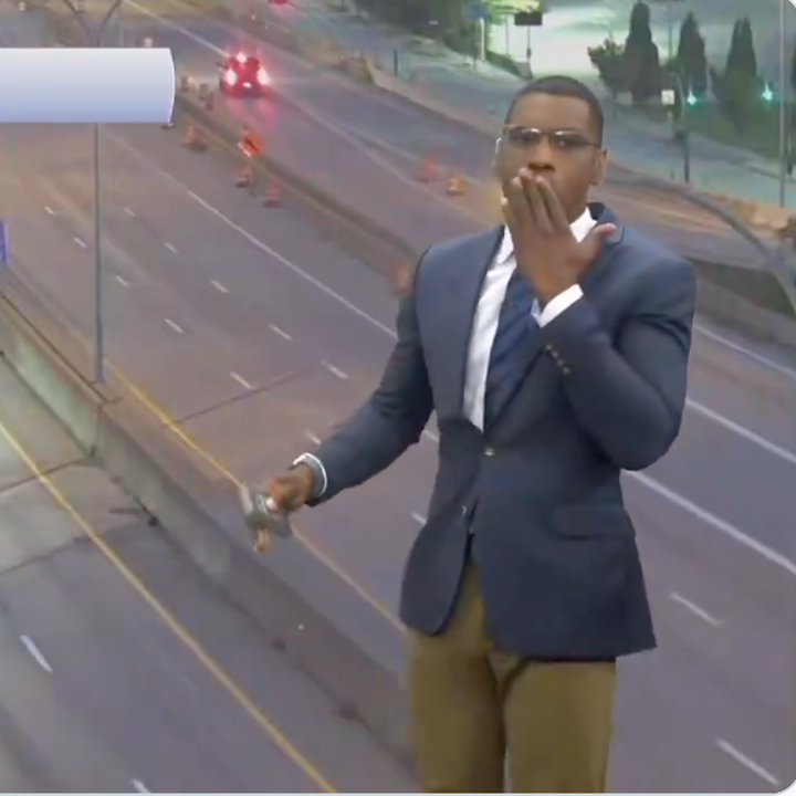 A person in a suit stands on a highway graphic, appearing surprised, possibly during a news segment