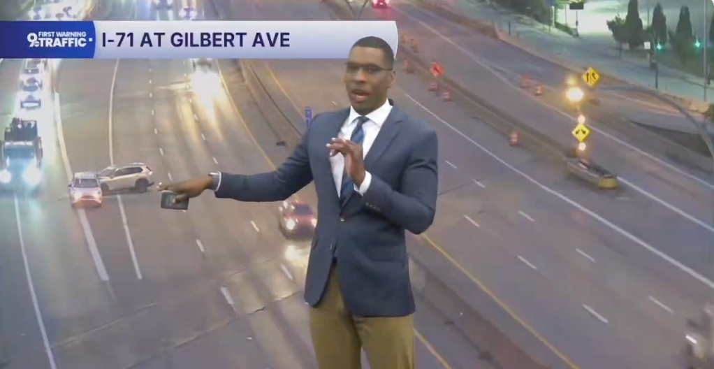 Trafikkreporter som presenterer live veiforhold på I-71 ved Gilbert Ave, med biler synlige på motorveiskjermene bak